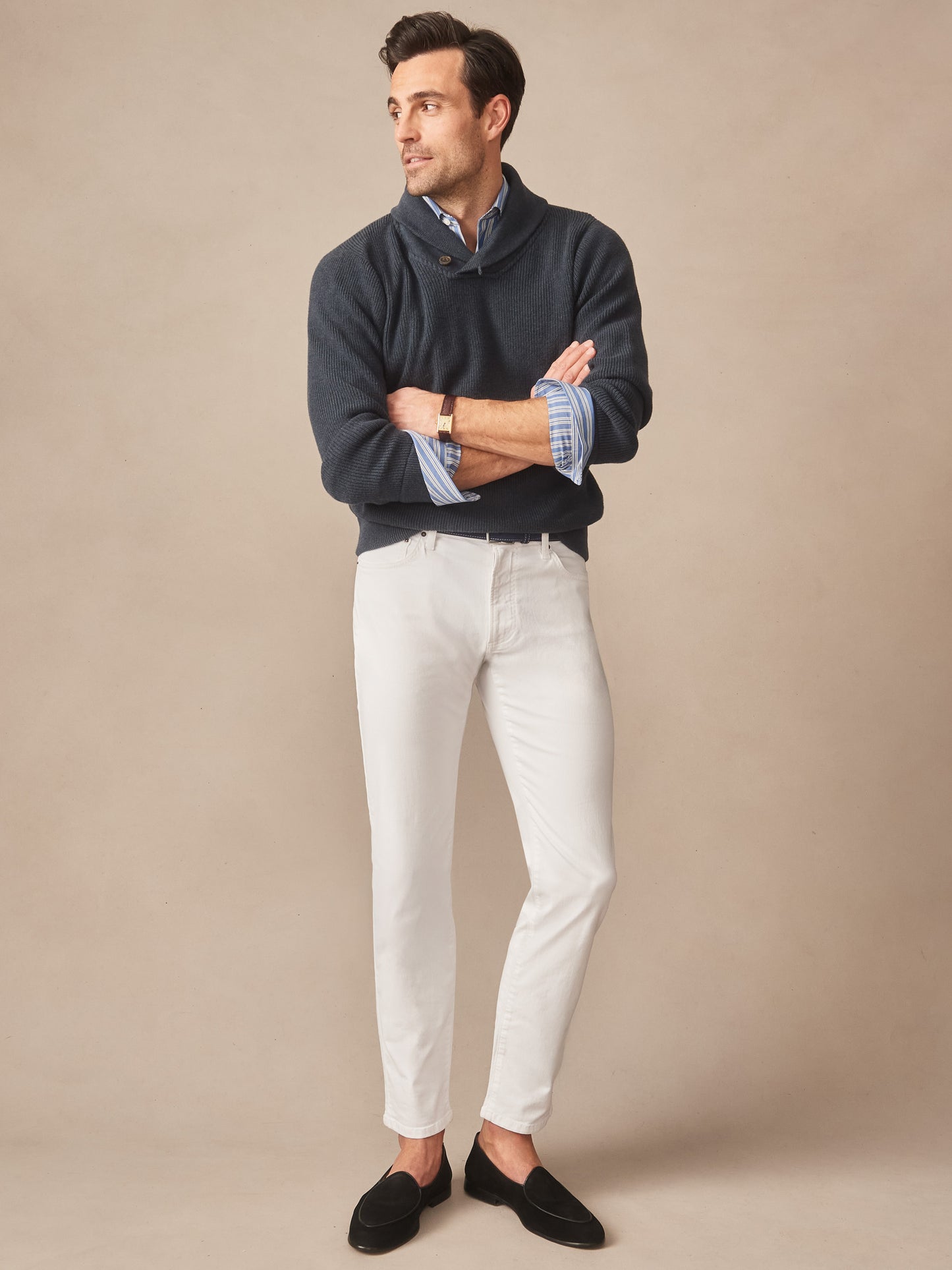 Man wearing a navy Hudson Sweater by J.McLaughlin layered over a blue striped shirt, paired with white pants and black loafers, showcasing effortlessly stylish, enduring designs with a legacy of timeless fashion. A destination for defining style. Life, Well-Lived.