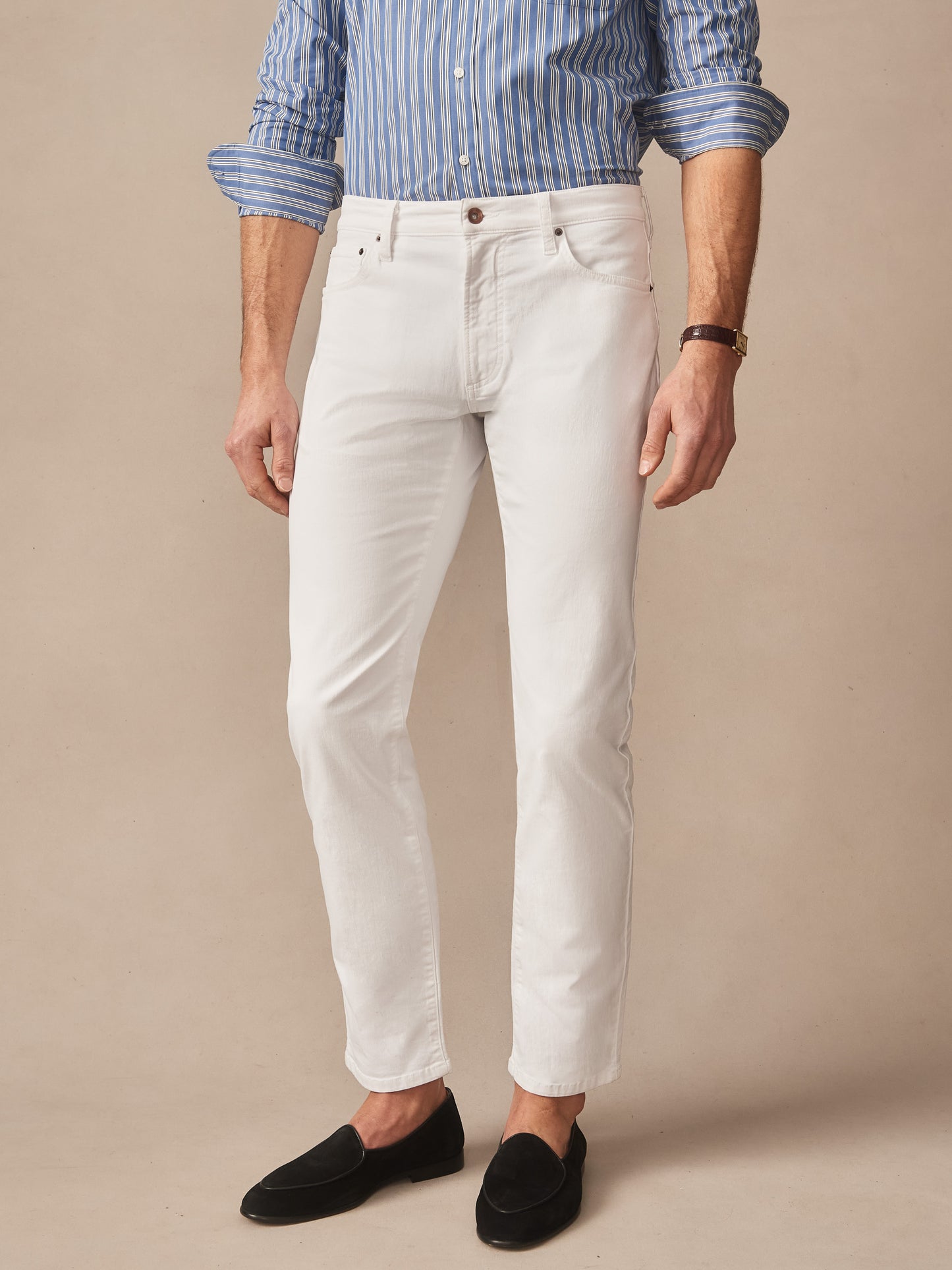 A man wearing Mercer Pants in white paired with a blue striped shirt and black loafers, showcasing J.McLaughlin's effortlessly stylish, enduring designs and innovative fabrics.