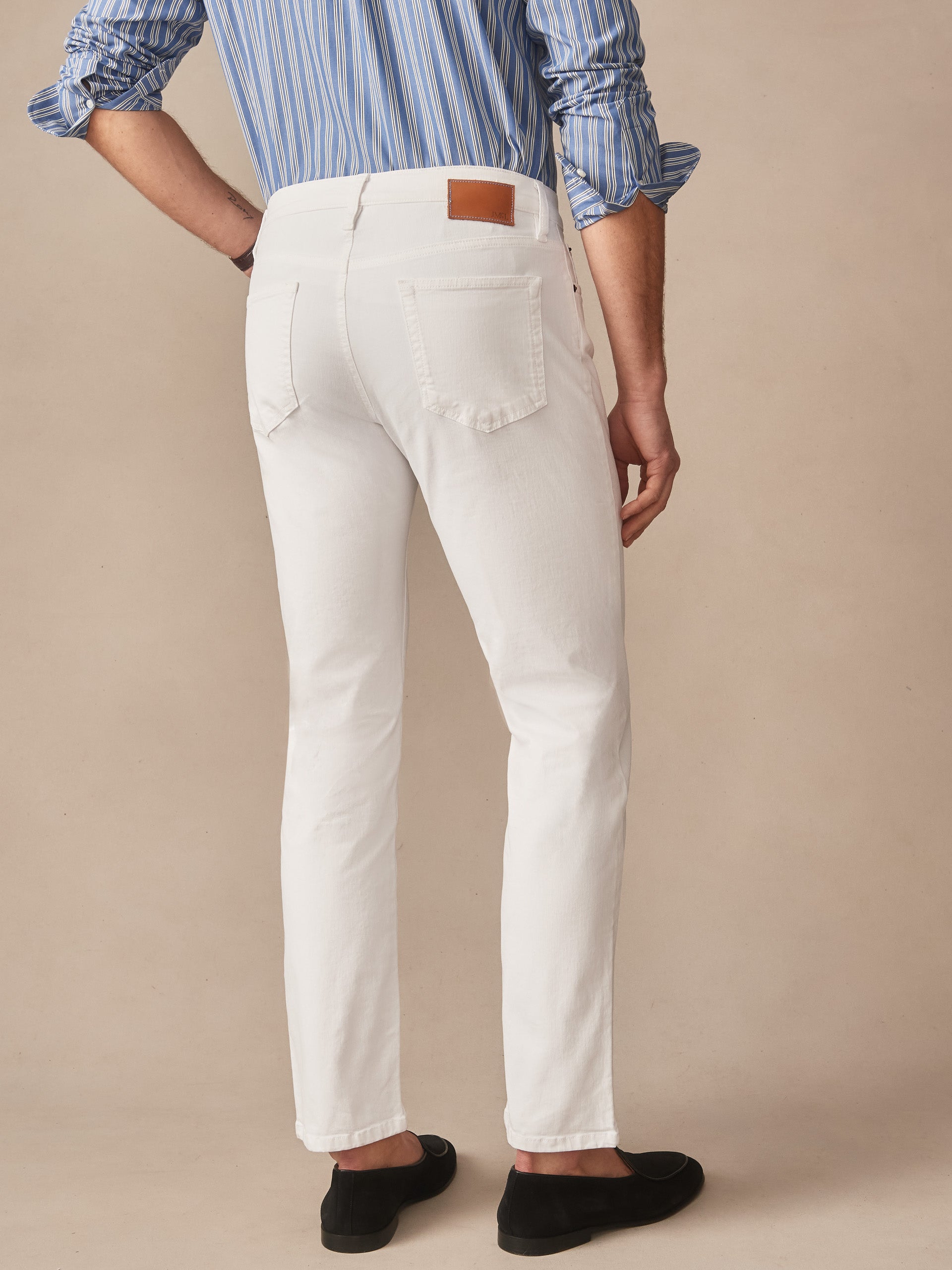 Man wearing white Mercer Pants by J.McLaughlin paired with a blue striped shirt and black loafers, showcasing effortlessly stylish, enduring designs and innovative fabrics.
