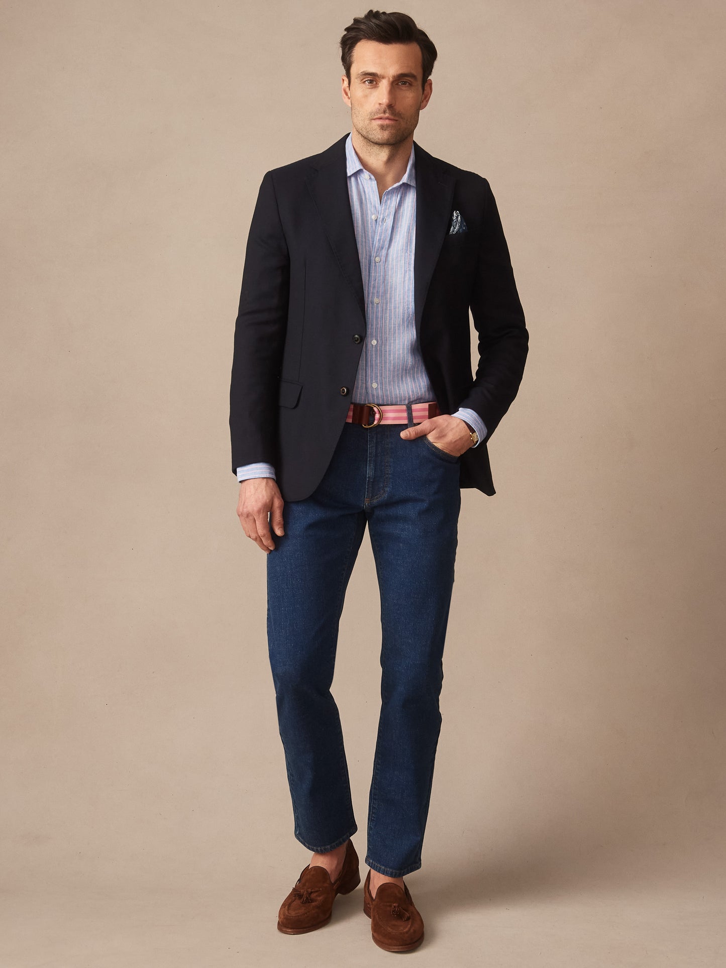 A man wearing a Suffolk Sport Coat by J.McLaughlin over a striped shirt with dark denim jeans and brown loafers, showcasing effortlessly stylish, enduring designs and innovative fabrics.