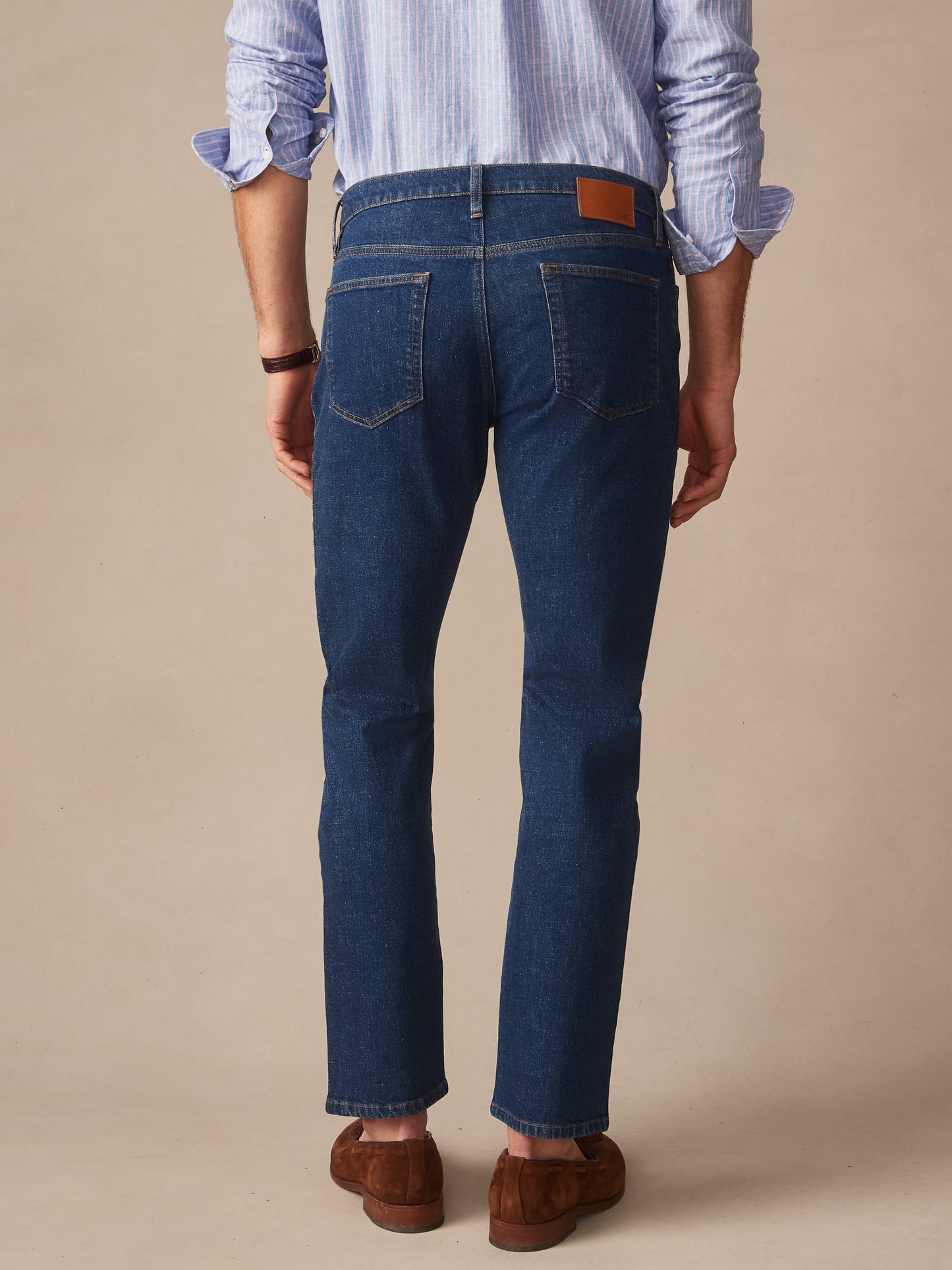 Man wearing Mercer Jeans in dark denim paired with a striped shirt and brown suede shoes, showcasing effortless style and enduring design by J.McLaughlin, a destination for defining style. Life, Well-Lived.