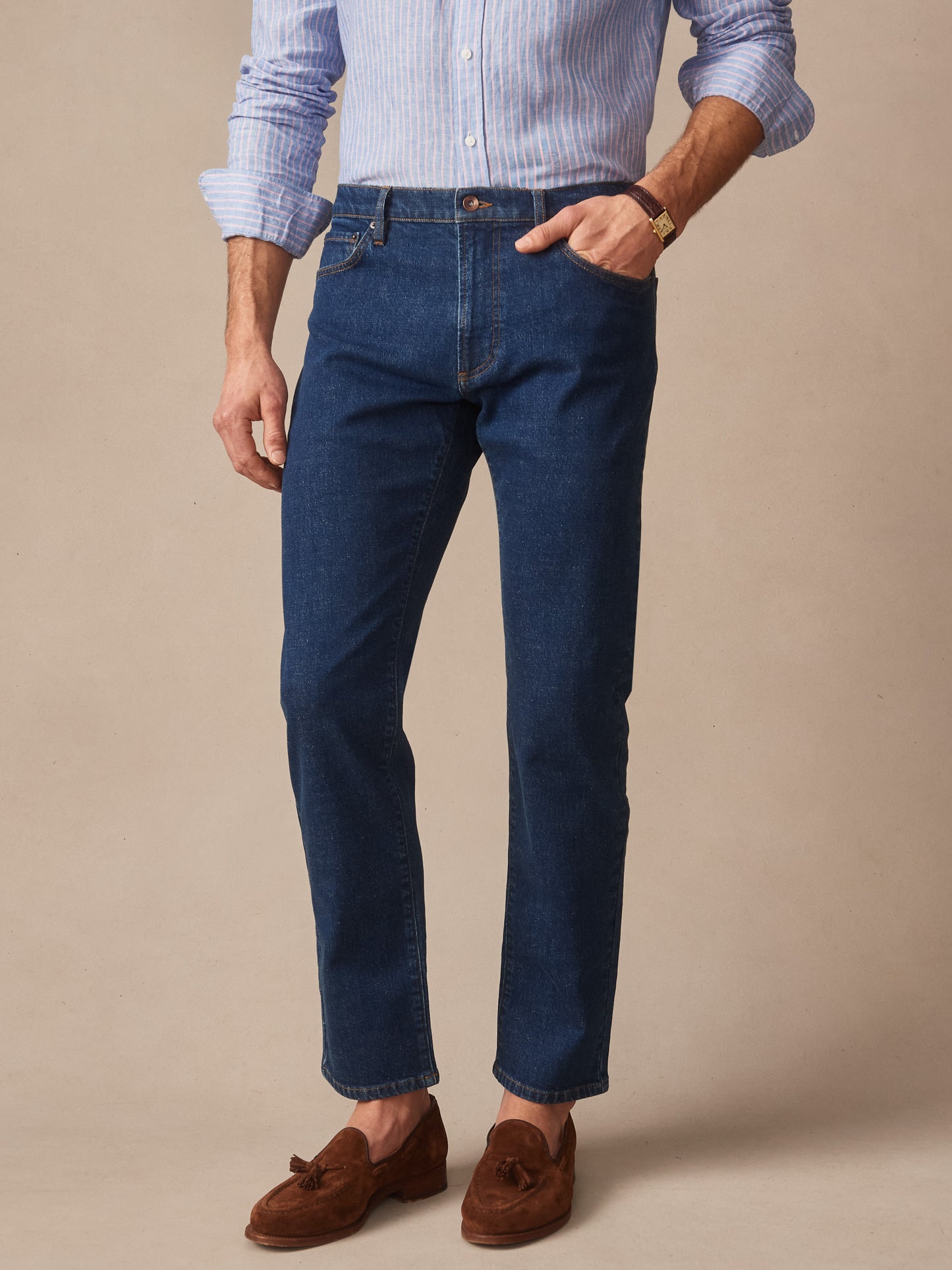 Man wearing dark denim Mercer Jeans by J.McLaughlin paired with a light blue striped shirt and brown suede loafers, showcasing effortlessly stylish, enduring designs and innovative fabrics.