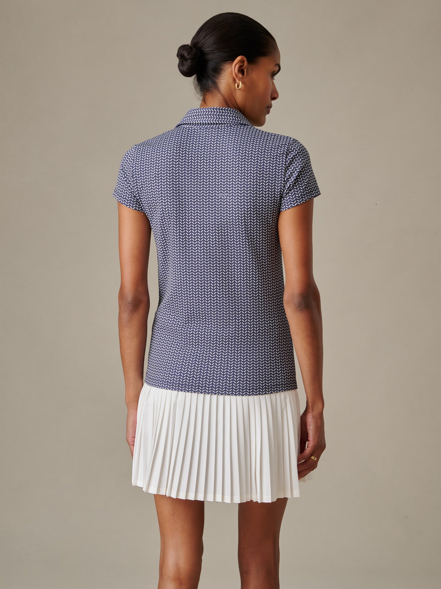 Woman wearing a J.McLaughlin Merlin Cap Sleeve Polo in Vine with a classic collar and a white pleated skirt, showcasing effortlessly stylish and enduring designs.