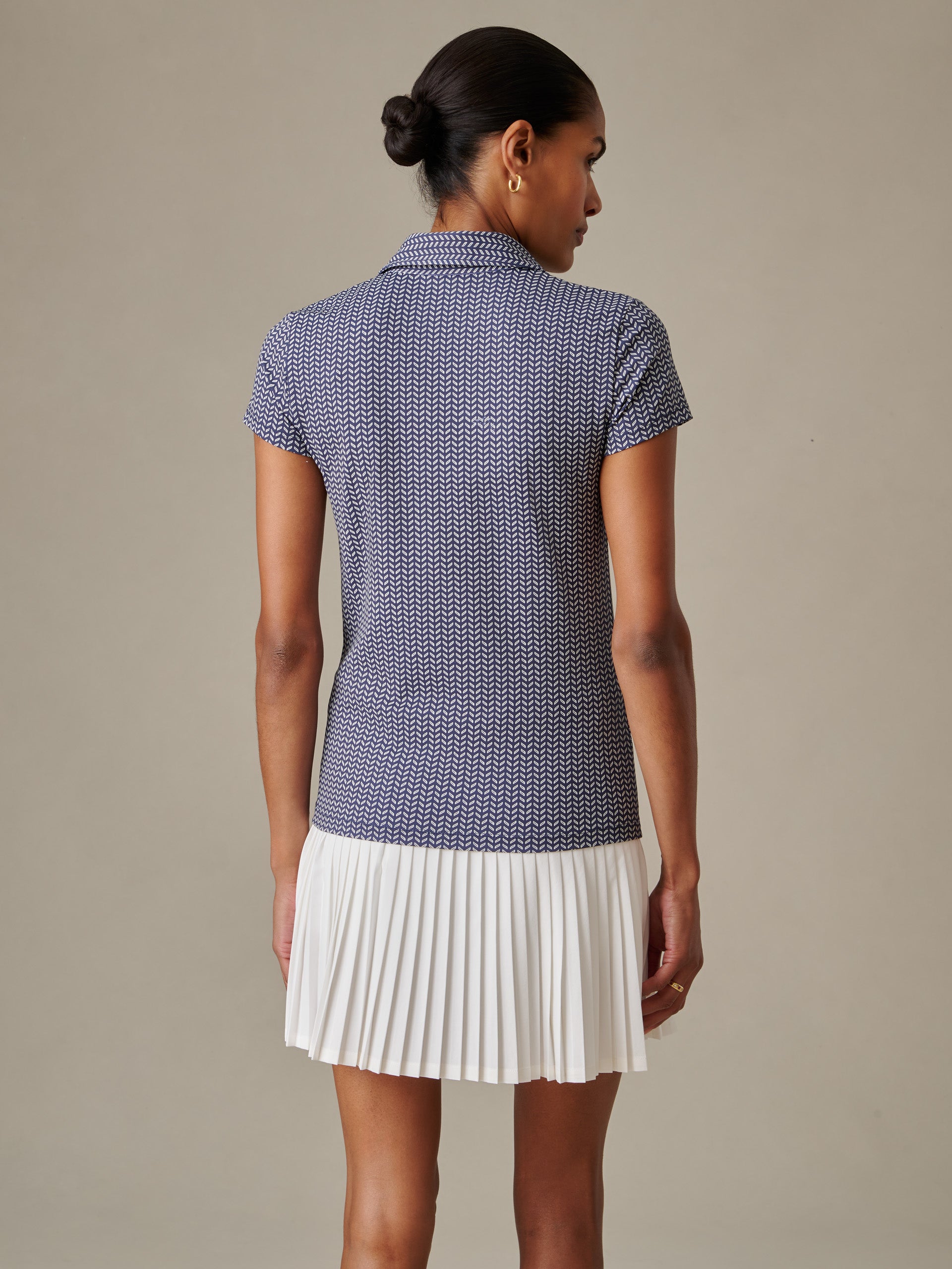 Woman wearing a J.McLaughlin Merlin Cap Sleeve Polo in Vine with a classic collar and a white pleated skirt, showcasing effortlessly stylish and enduring designs.