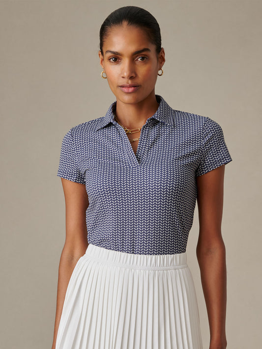 Woman wearing a patterned Merlin Cap Sleeve Polo in Vine by J.McLaughlin, paired with a white pleated skirt, showcasing effortlessly stylish and enduring designs.