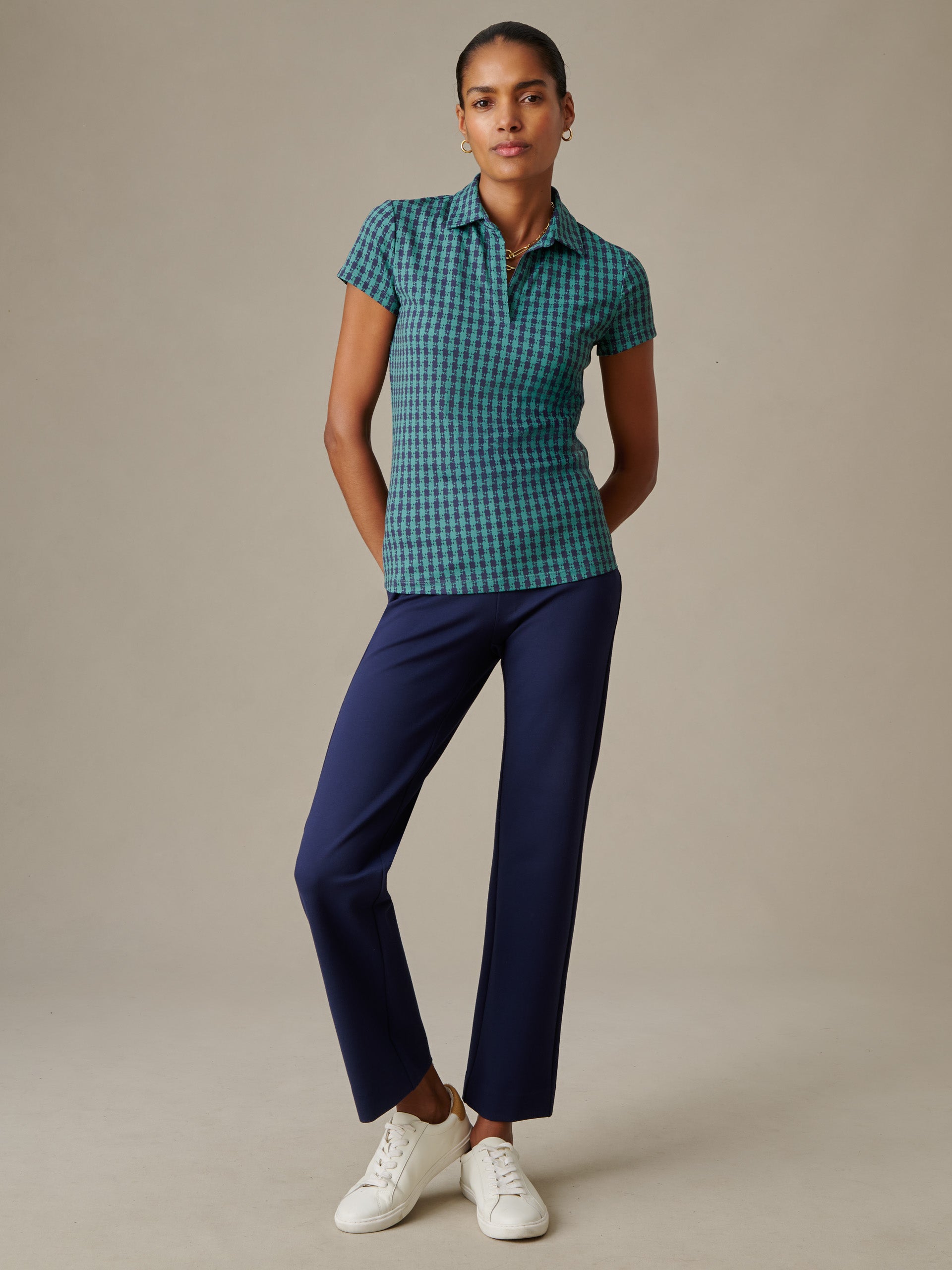 Woman wearing a Merlin Cap Sleeve Polo in Algiers Check by J.McLaughlin paired with navy pants and white sneakers, showcasing effortlessly stylish, enduring designs.