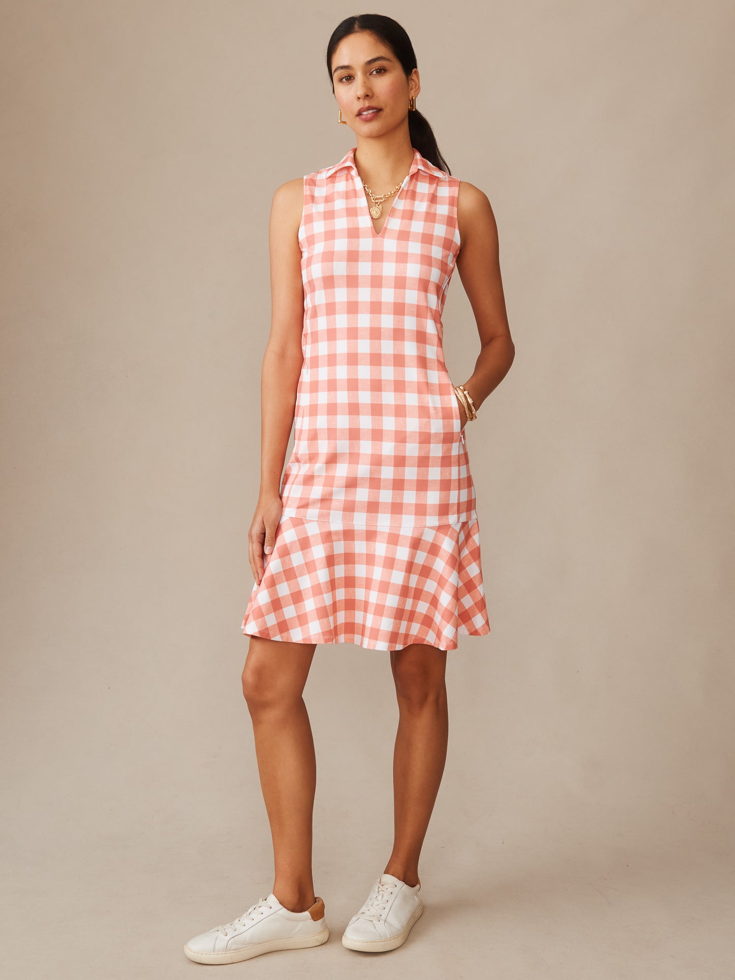 Woman wearing a sleeveless Merlin Dress in Textured Gingham by J.McLaughlin in soft coral and white, styled effortlessly with simple jewelry and white sneakers, showcasing enduring designs and innovative fabrics from a destination for defining style. Life, Well-Lived.