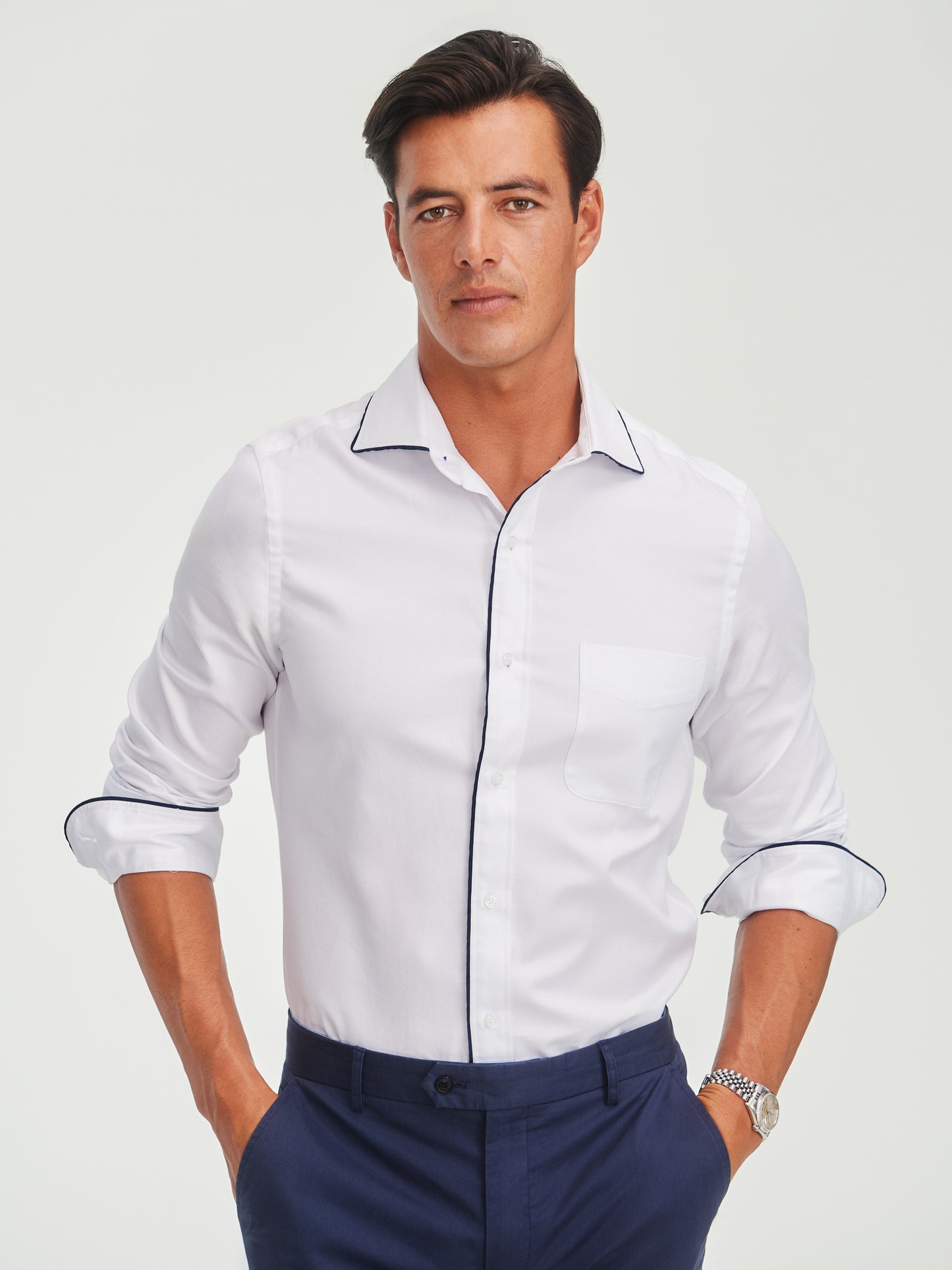 Man wearing a white Anderson Cotton Shirt by J.McLaughlin with dark piping detail, paired with navy pants, showcasing effortlessly stylish, enduring designs and innovative fabrics for a legacy of timeless fashion.