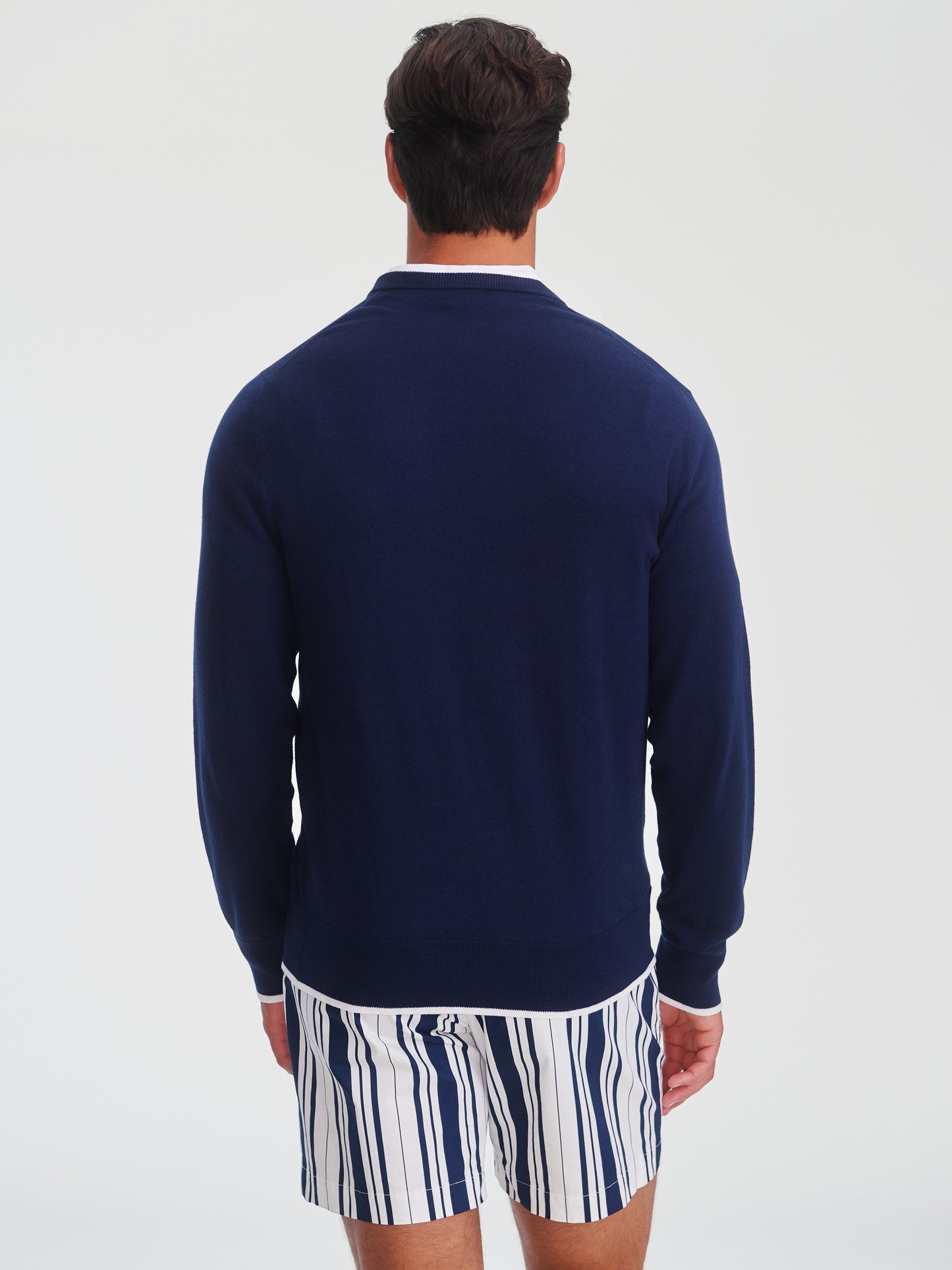 Man wearing a navy Doug Sweater by J.McLaughlin, paired with striped shorts, showcasing an effortlessly stylish look with enduring designs and innovative fabrics.