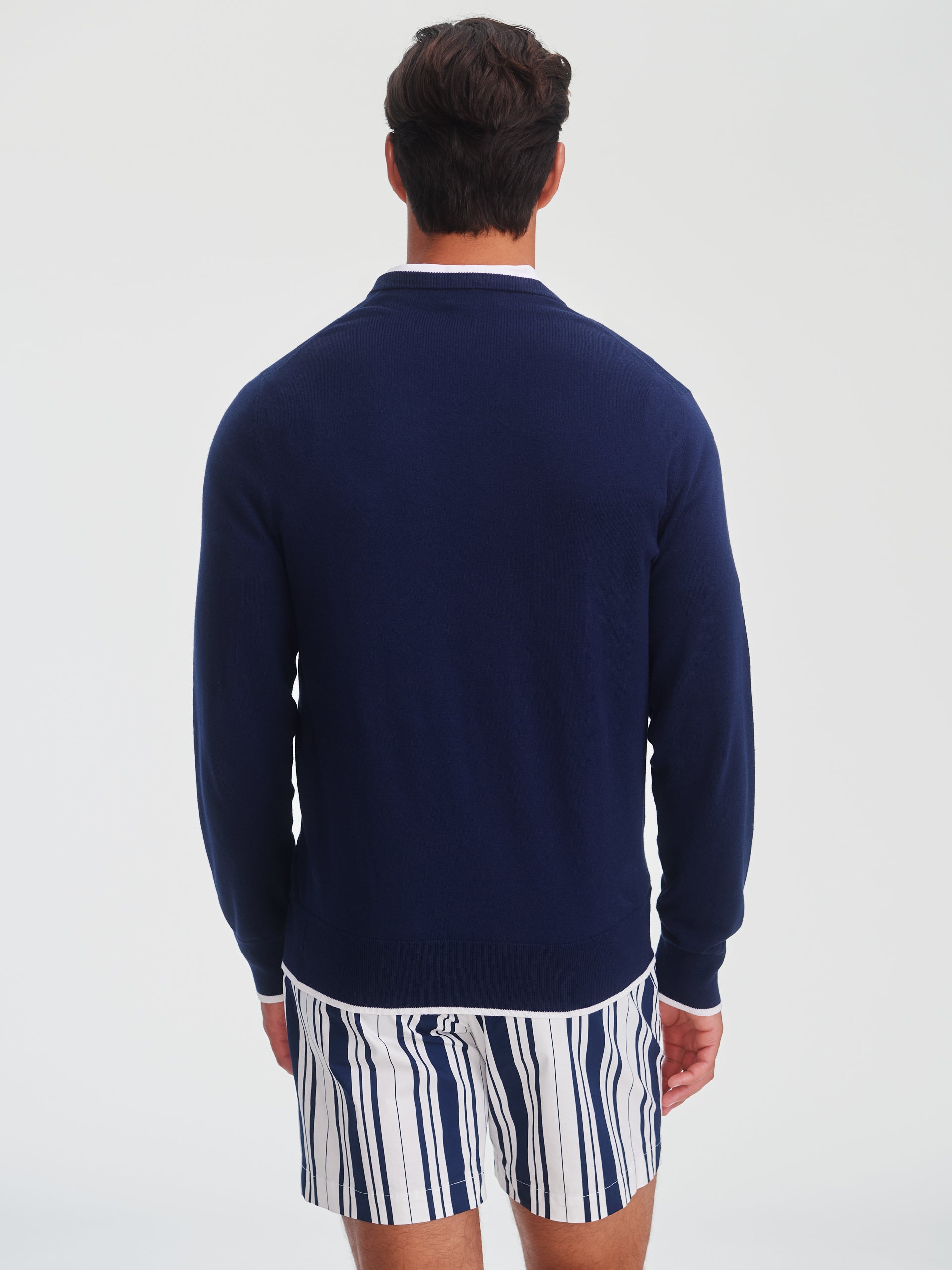 Man wearing a navy Doug Sweater by J.McLaughlin, paired with striped shorts, showcasing an effortlessly stylish look with enduring designs and innovative fabrics.