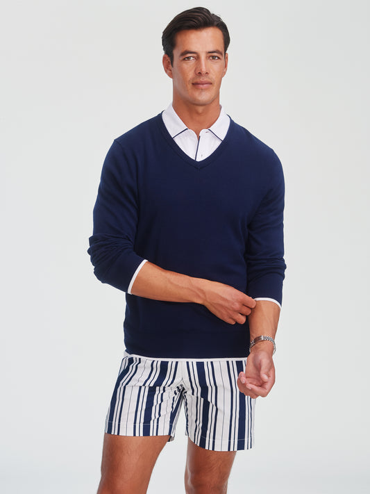 Man wearing a navy Doug Sweater by J.McLaughlin over a white collared shirt paired with striped shorts, showcasing effortlessly stylish, enduring designs in classic menswear.