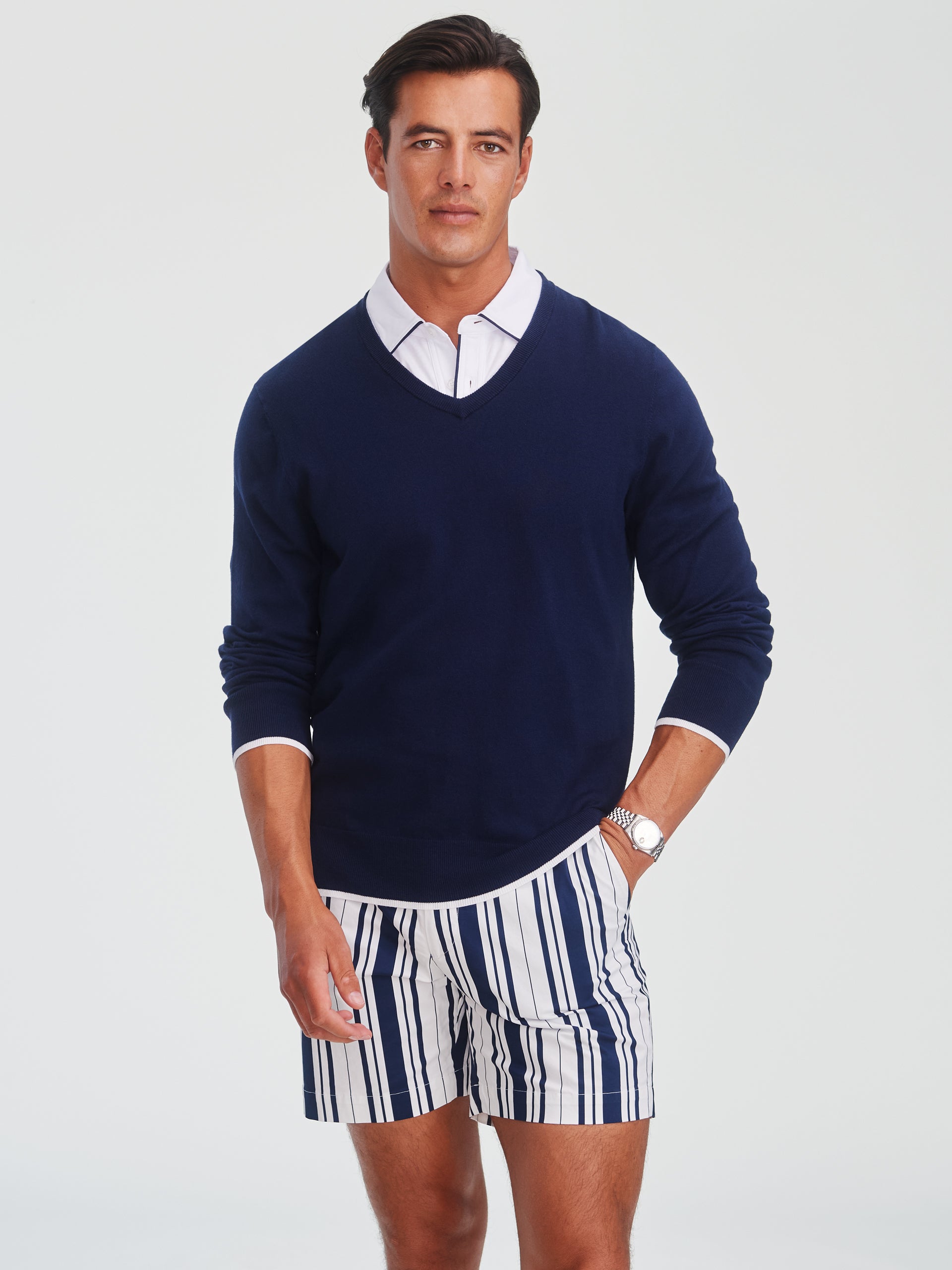 Man wearing a navy Doug Sweater over a white collared shirt paired with striped shorts, showcasing J.McLaughlin's effortlessly stylish sweater with enduring designs and innovative fabrics.