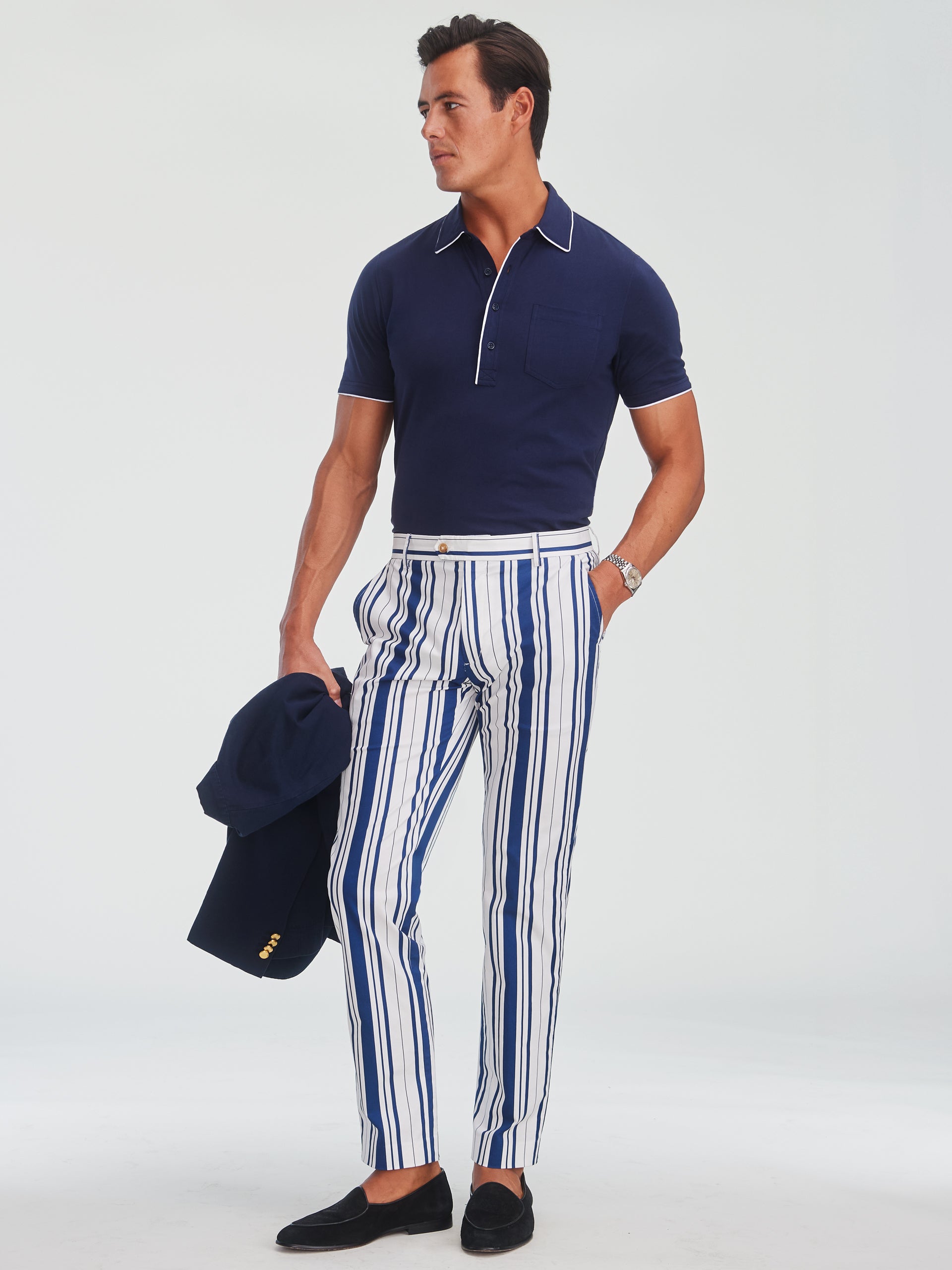 Man wearing J.McLaughlin Madison Fancy Pants in Mariner Stripe paired with a navy short-sleeve polo, holding a navy blazer, showcasing effortlessly stylish and enduring designs in innovative fabrics.