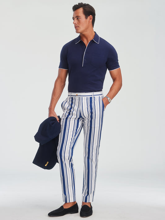 Man wearing J.McLaughlin Madison Fancy Pants in Mariner Stripe paired with a navy short-sleeve polo, holding a navy blazer, showcasing effortlessly stylish and enduring designs in innovative fabrics.