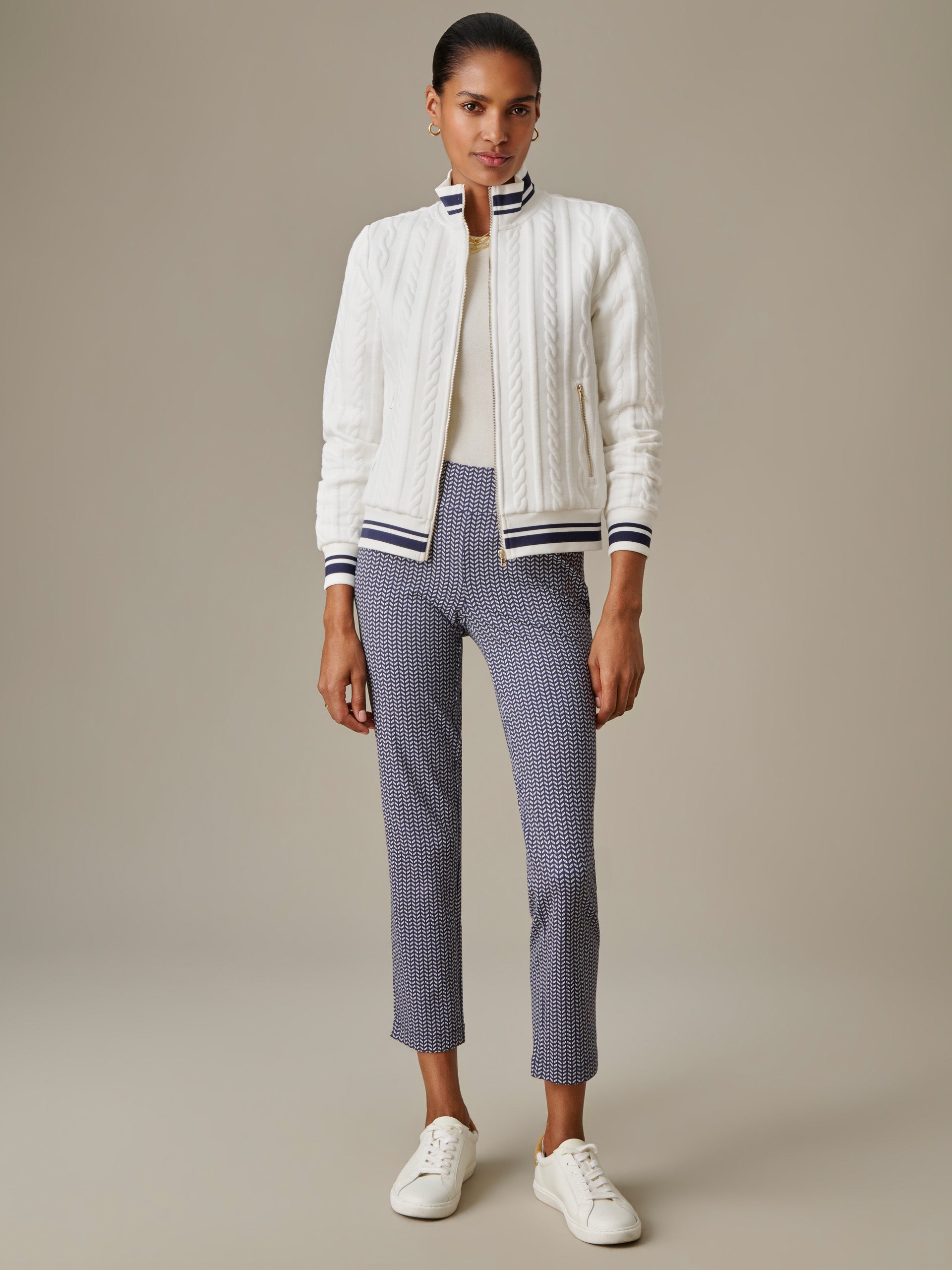 Woman wearing a white Willa Jacket in Cable Jacquard by J.McLaughlin, paired with patterned slim pants and white sneakers, showcasing effortless style and enduring design.