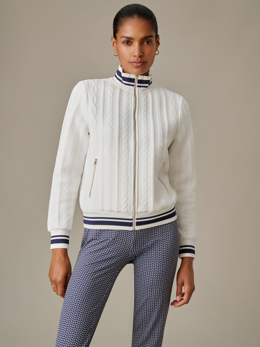 Model wearing a white Willa Jacket in Cable Jacquard by J.McLaughlin featuring a zip front, cable knit texture, and striped collar and cuffs, styled with patterned pants.