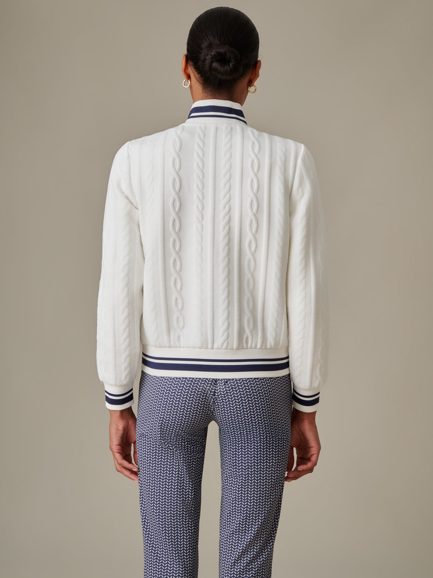 Model wearing the Willa Jacket in Cable Jacquard by J.McLaughlin, showcasing an effortlessly stylish white cable-knit jacket with striped collar and cuffs paired with patterned pants.