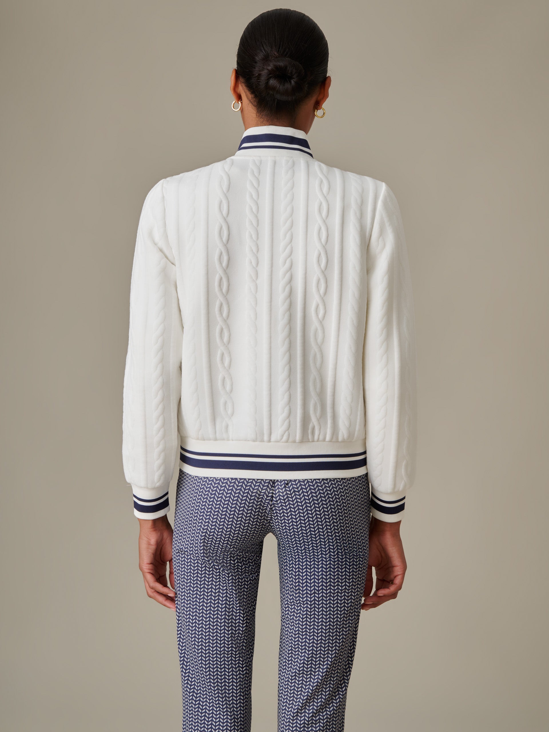 Model wearing the Willa Jacket in Cable Jacquard by J.McLaughlin, showcasing an effortlessly stylish white cable-knit jacket with striped collar and cuffs paired with patterned pants.