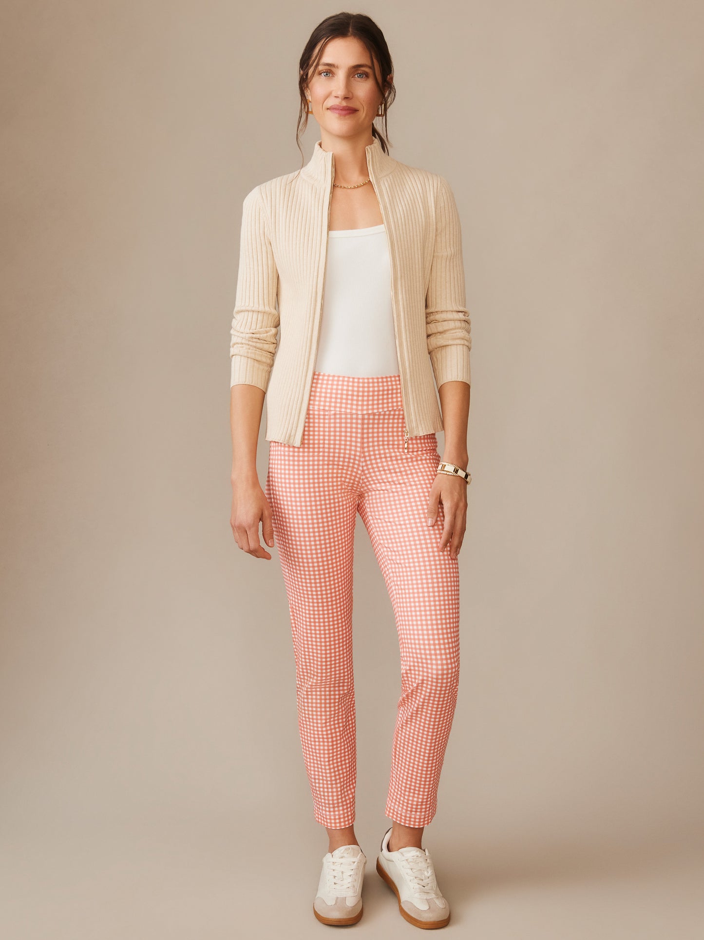 A stylish woman models Newport Capri Pants in Midi Cabana Gingham by J.McLaughlin, paired with a cream ribbed jacket and white top, showcasing effortlessly stylish, enduring designs.