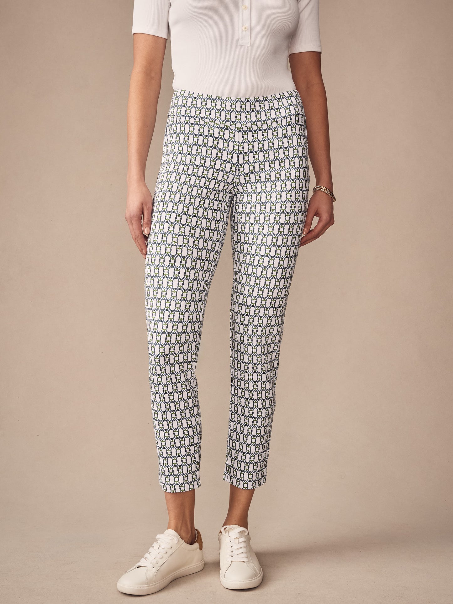 A model wearing J.McLaughlin Newport Capri Pants in Signet Lock, featuring a white base with a blue and green geometric pattern, paired with white sneakers and a simple white top.