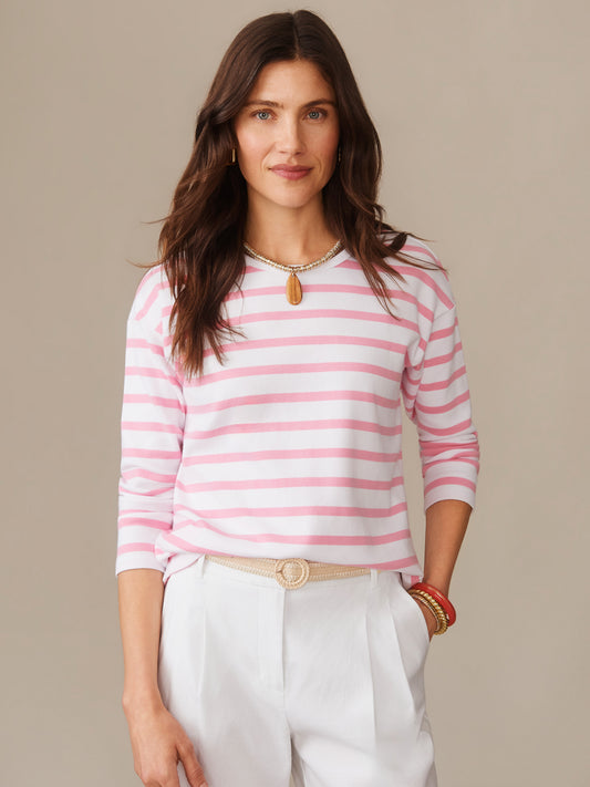 Woman wearing a J. McLaughlin Nico Tee in Stripe with soft pink and white horizontal stripes, paired with white pants and accessorized with a necklace and bracelets, showcasing effortlessly stylish, enduring designs and innovative fabrics from a destination for defining style. Life, Well-Lived.