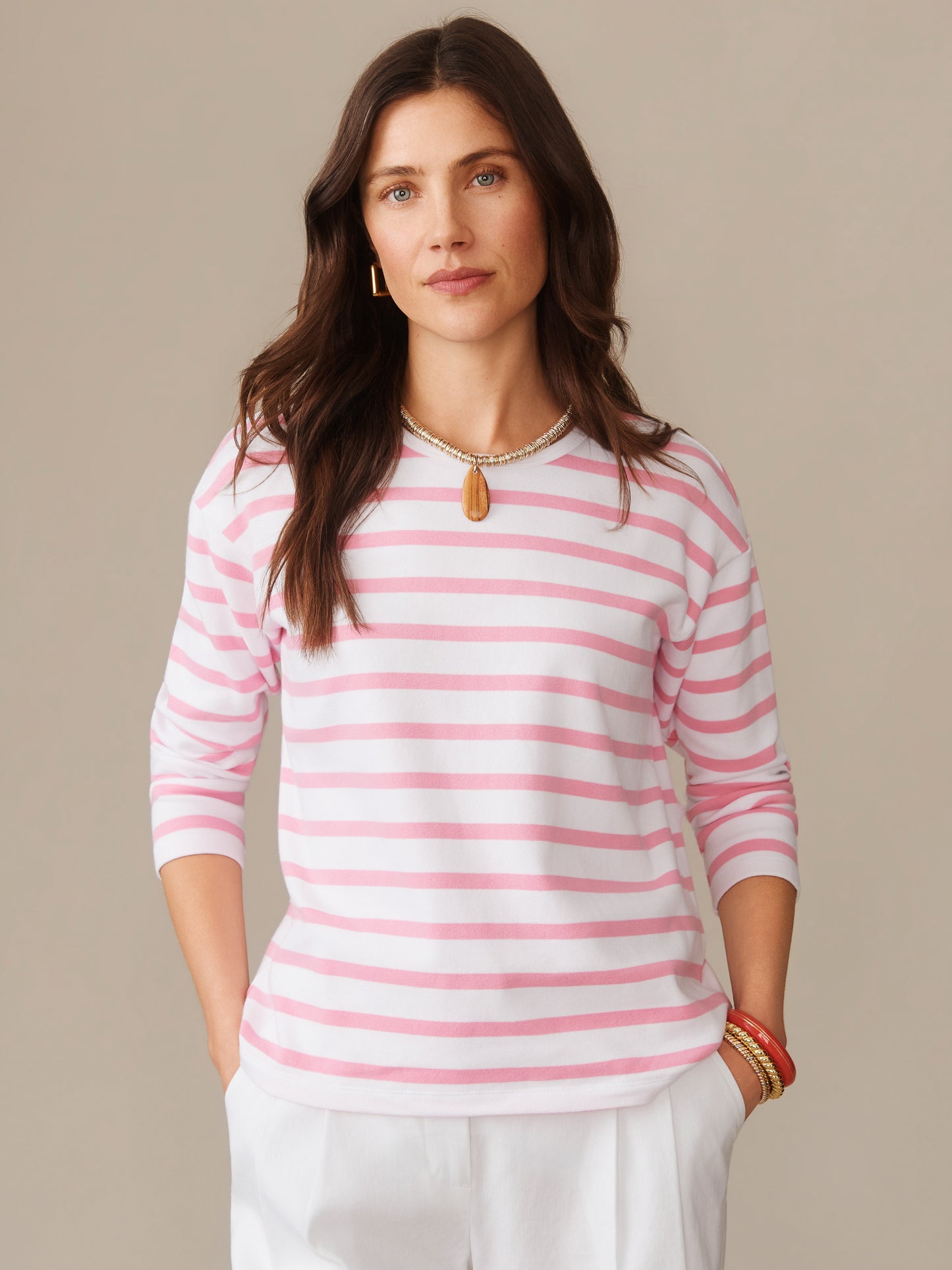 Woman wearing a Nico Tee in Stripe by J.McLaughlin featuring soft pink and white stripes, styled with white pants and accessories, showcasing effortlessly stylish, enduring designs and innovative fabrics. A destination for defining style. Life, Well-Lived.