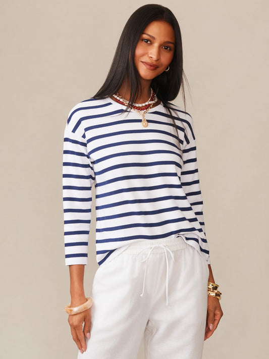 Woman wearing a Nico Tee in Stripe by J.McLaughlin, featuring navy and white stripes, styled with white pants and layered necklaces, embodying effortlessly stylish, enduring designs in innovative fabrics. A destination for defining style. Life, Well-Lived.