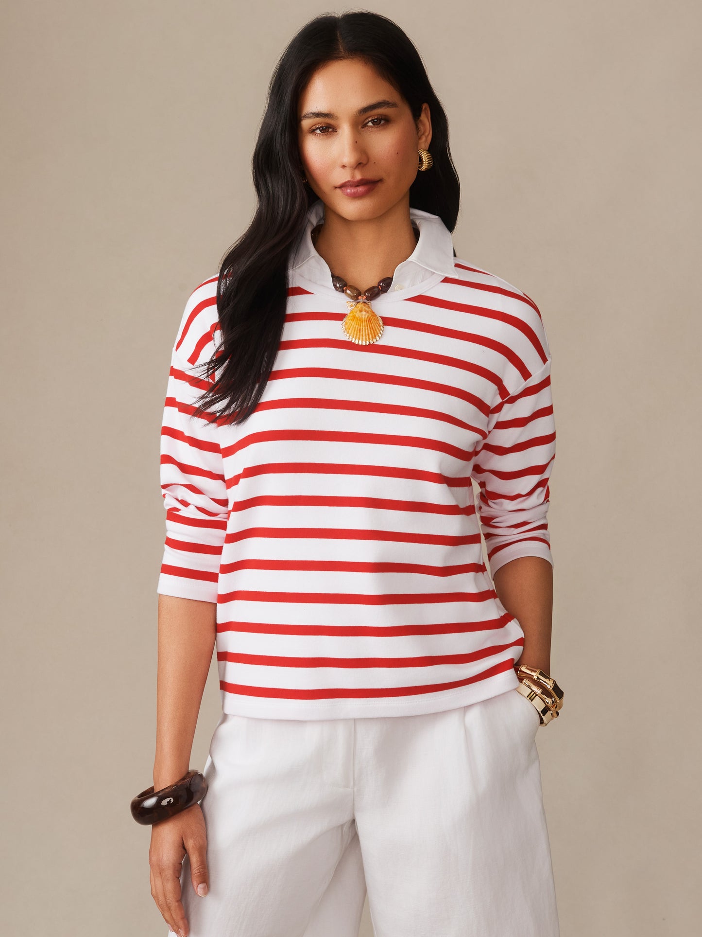 Woman wearing J.McLaughlin Nico Tee in Stripe with red and white stripes, layered over a white collared shirt, styled with gold earrings and bracelets, embodying effortlessly stylish, enduring designs for a life well-lived.