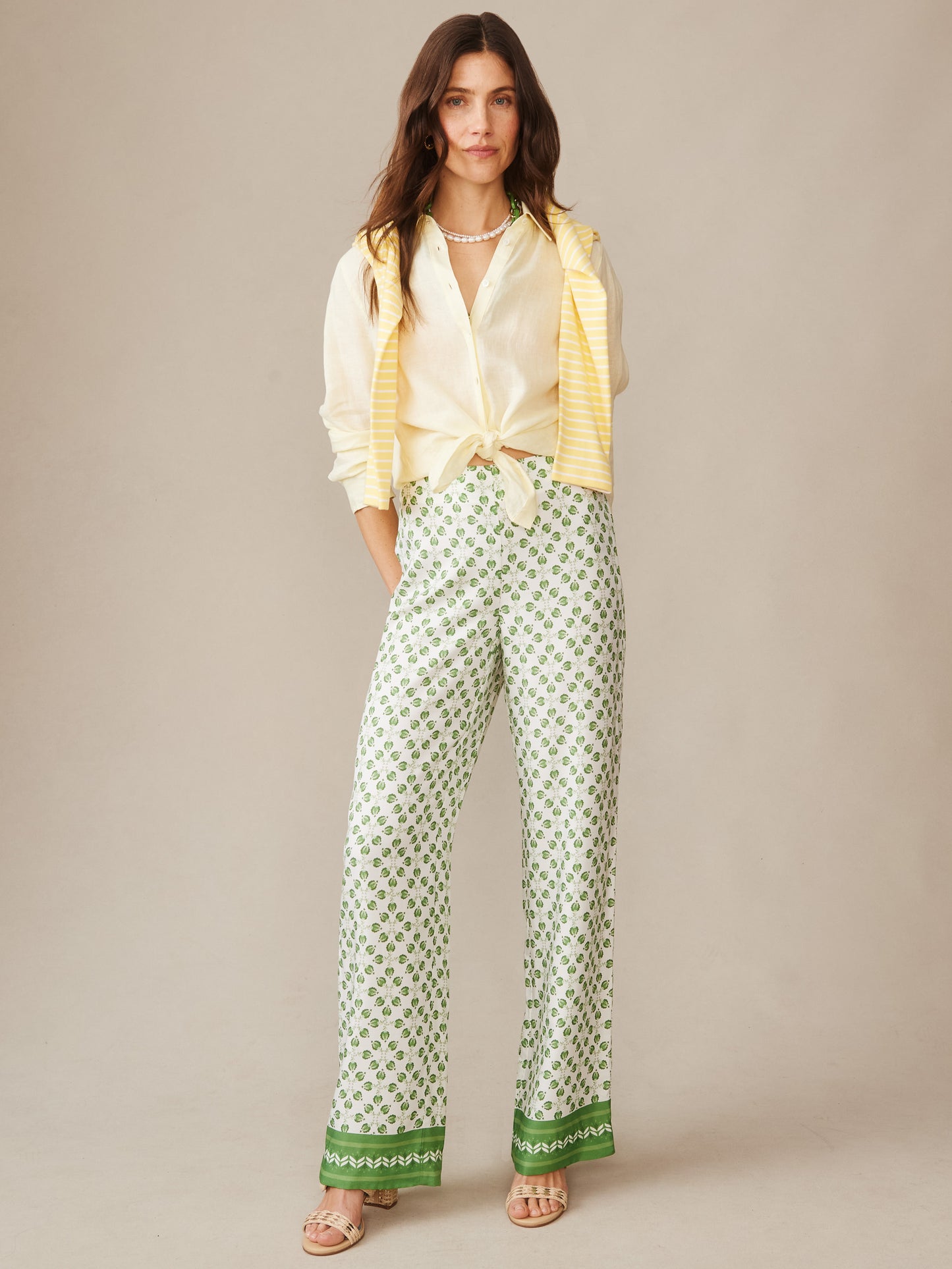 Woman wearing Carter Silk Blend Pants in Mythic Geo Border by J.McLaughlin, styled with a tied cream blouse and yellow striped sweater, showcasing effortlessly stylish pants with enduring designs and innovative fabrics. A destination for defining style. Life, Well-Lived.