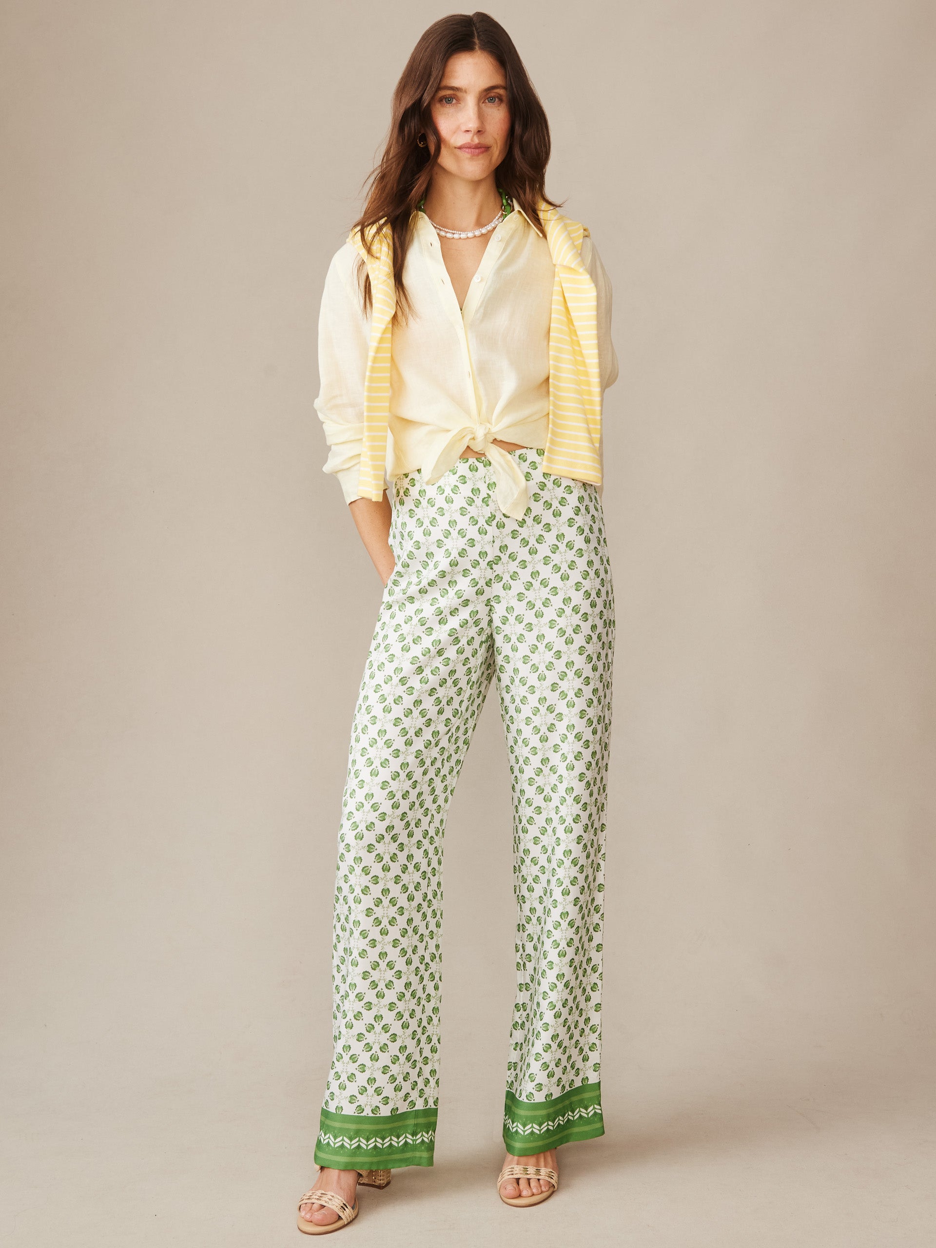 Woman wearing Carter Silk Blend Pants in Mythic Geo Border by J.McLaughlin, styled with a tied cream blouse and yellow striped sweater, showcasing effortlessly stylish pants with enduring designs and innovative fabrics. A destination for defining style. Life, Well-Lived.