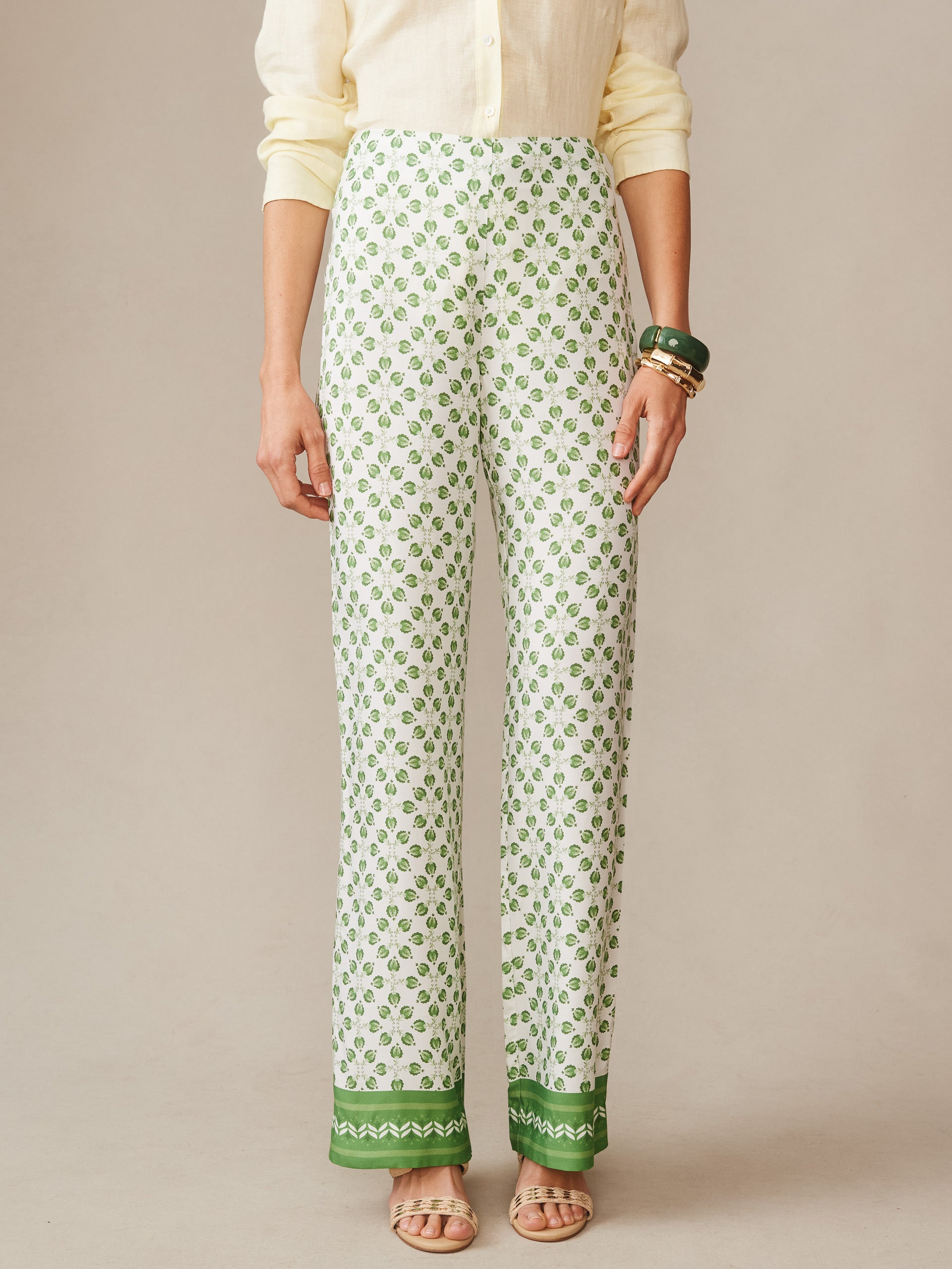 Model wearing Carter Silk Blend Pants in Mythic Geo Border by J.McLaughlin, featuring a green geometric pattern with contrasting green borders, paired with a light blouse and bracelets, embodying effortlessly stylish, enduring designs and innovative fabrics from a destination for defining style. Life, Well-Lived.