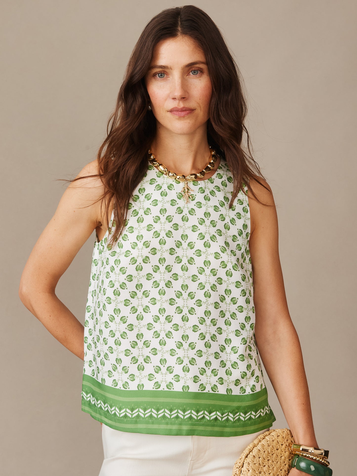 Woman wearing Norie Silk Blend Blouse in Mythic Geo Border with green geometric pattern and border, styled with chunky gold necklace and carrying a woven bag, by J.McLaughlin. Effortlessly stylish with enduring designs and innovative fabrics, a destination for defining style. Life, Well-Lived.