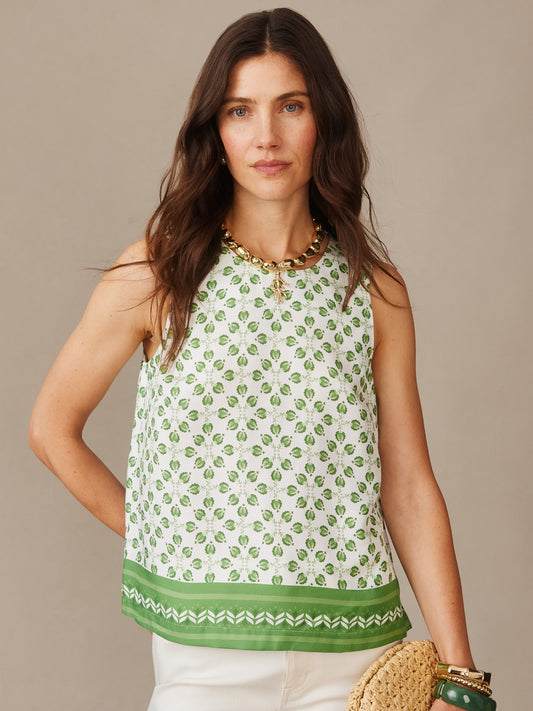 Woman wearing Norie Silk Blend Blouse in Mythic Geo Border with green geometric pattern and border, styled with chunky gold necklace and carrying a woven bag, by J.McLaughlin. Effortlessly stylish with enduring designs and innovative fabrics, a destination for defining style. Life, Well-Lived.