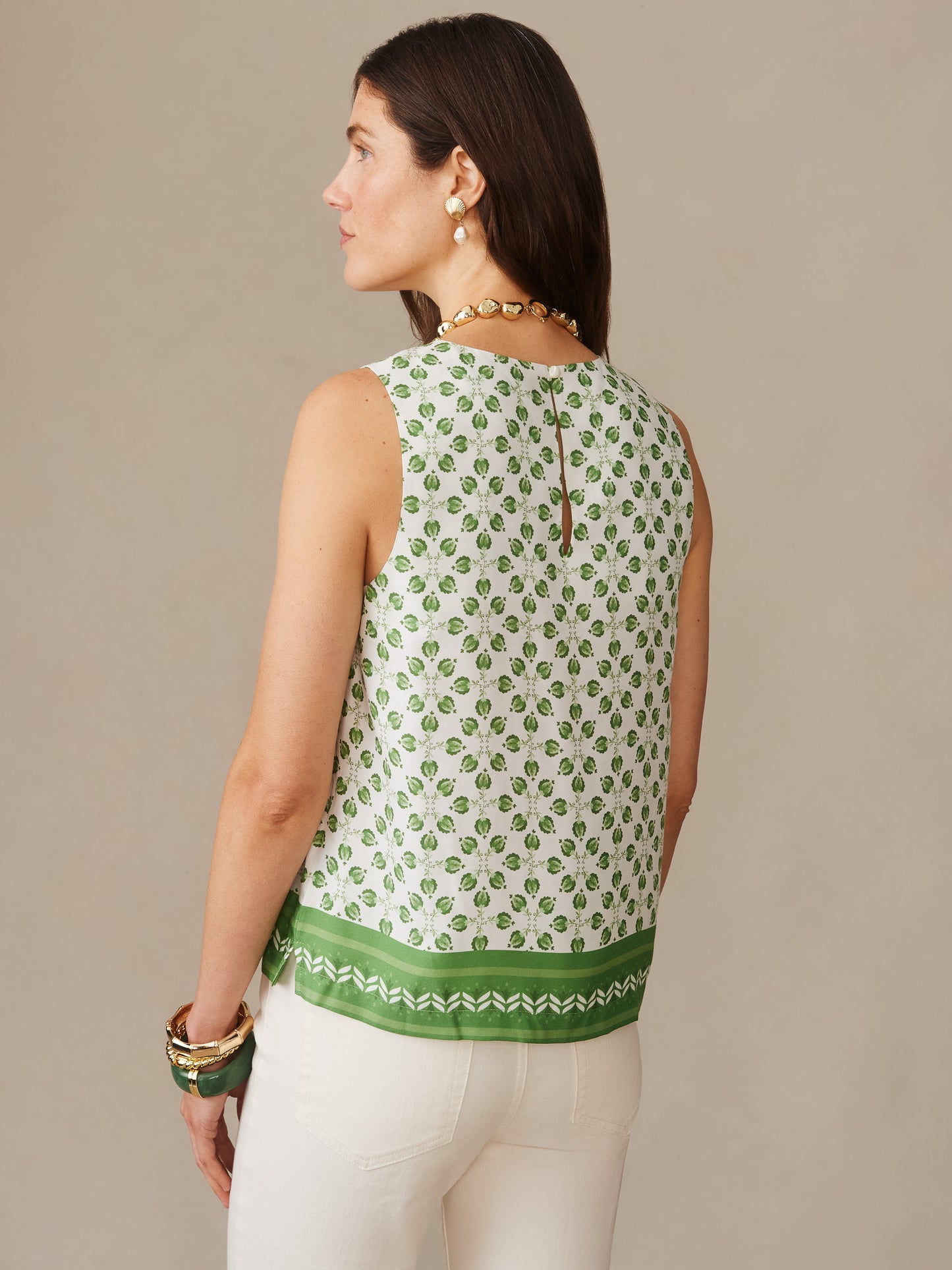 Woman wearing Norie Silk Blend Blouse in Mythic Geo Border, featuring a white and green geometric pattern, styled with white pants and gold jewelry by J.McLaughlin. Effortlessly stylish, enduring designs crafted from innovative fabrics, embodying a legacy of timeless fashion. A destination for defining style. Life, Well-Lived.
