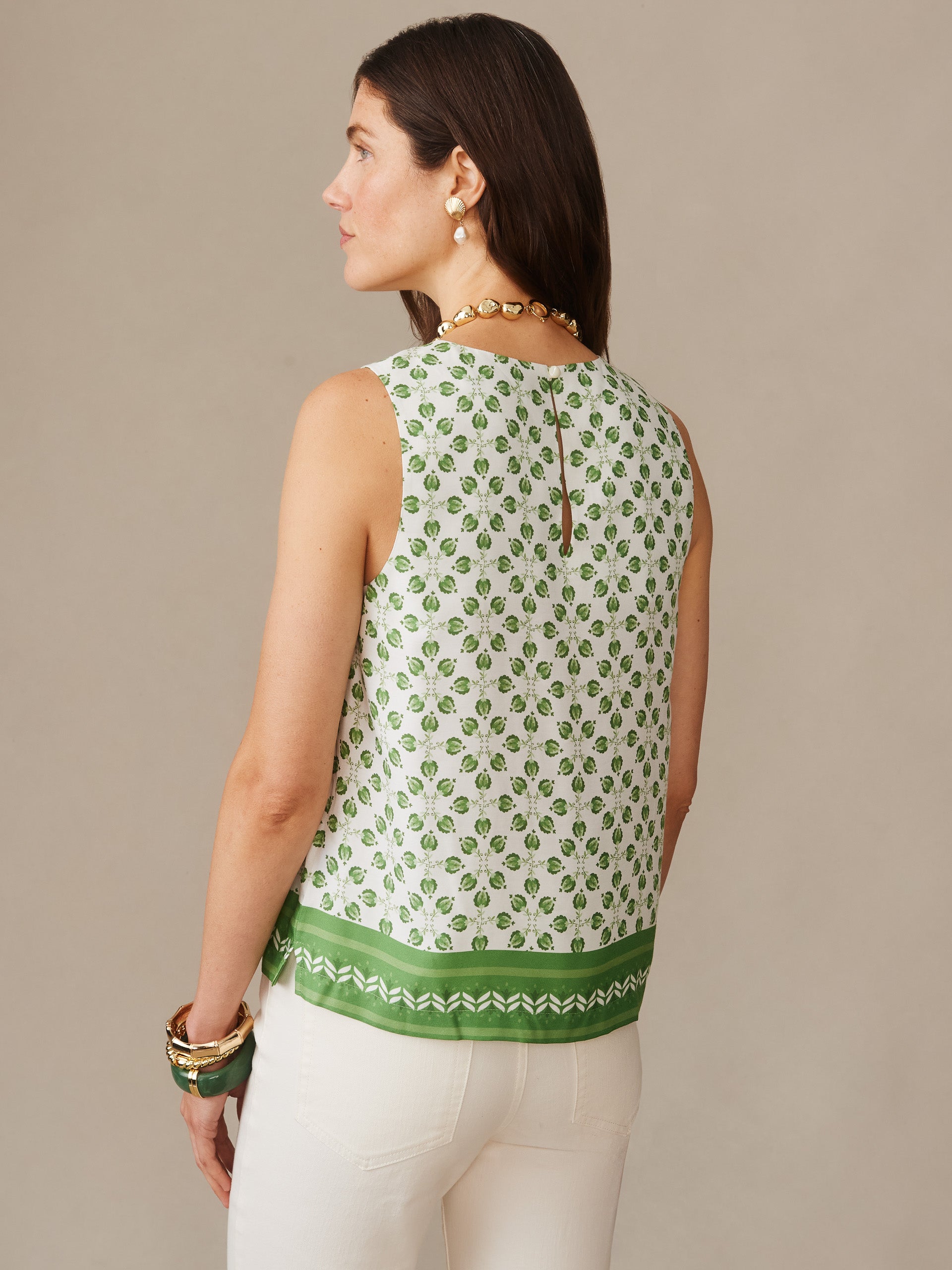 Woman wearing Norie Silk Blend Blouse in Mythic Geo Border, featuring a white and green geometric pattern, styled with white pants and gold jewelry by J.McLaughlin. Effortlessly stylish, enduring designs crafted from innovative fabrics, embodying a legacy of timeless fashion. A destination for defining style. Life, Well-Lived.