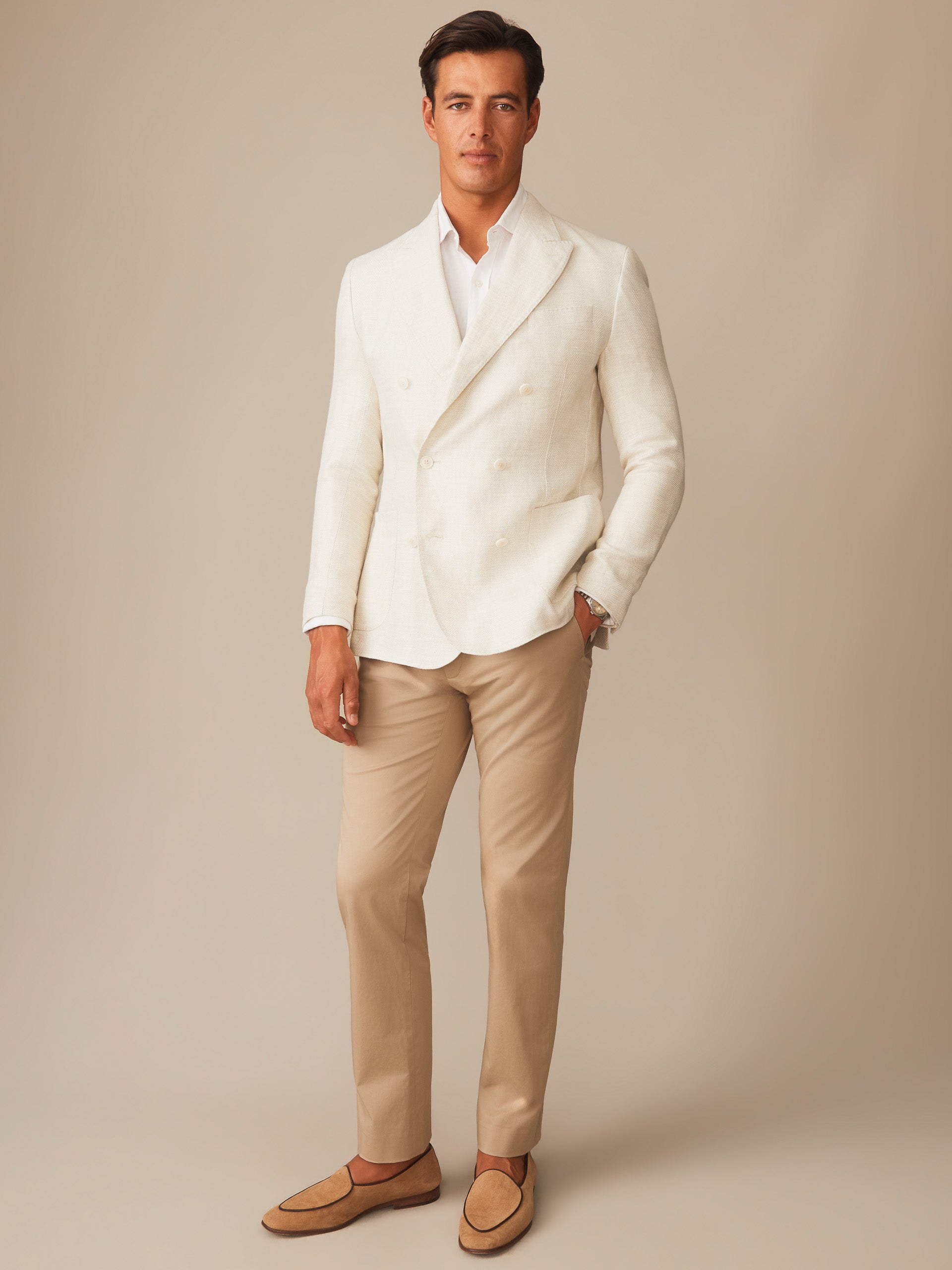 Man wearing a white double-breasted Notting Blazer by J.McLaughlin paired with beige pants and loafers, embodying effortlessly stylish and enduring designs for a life well-lived.