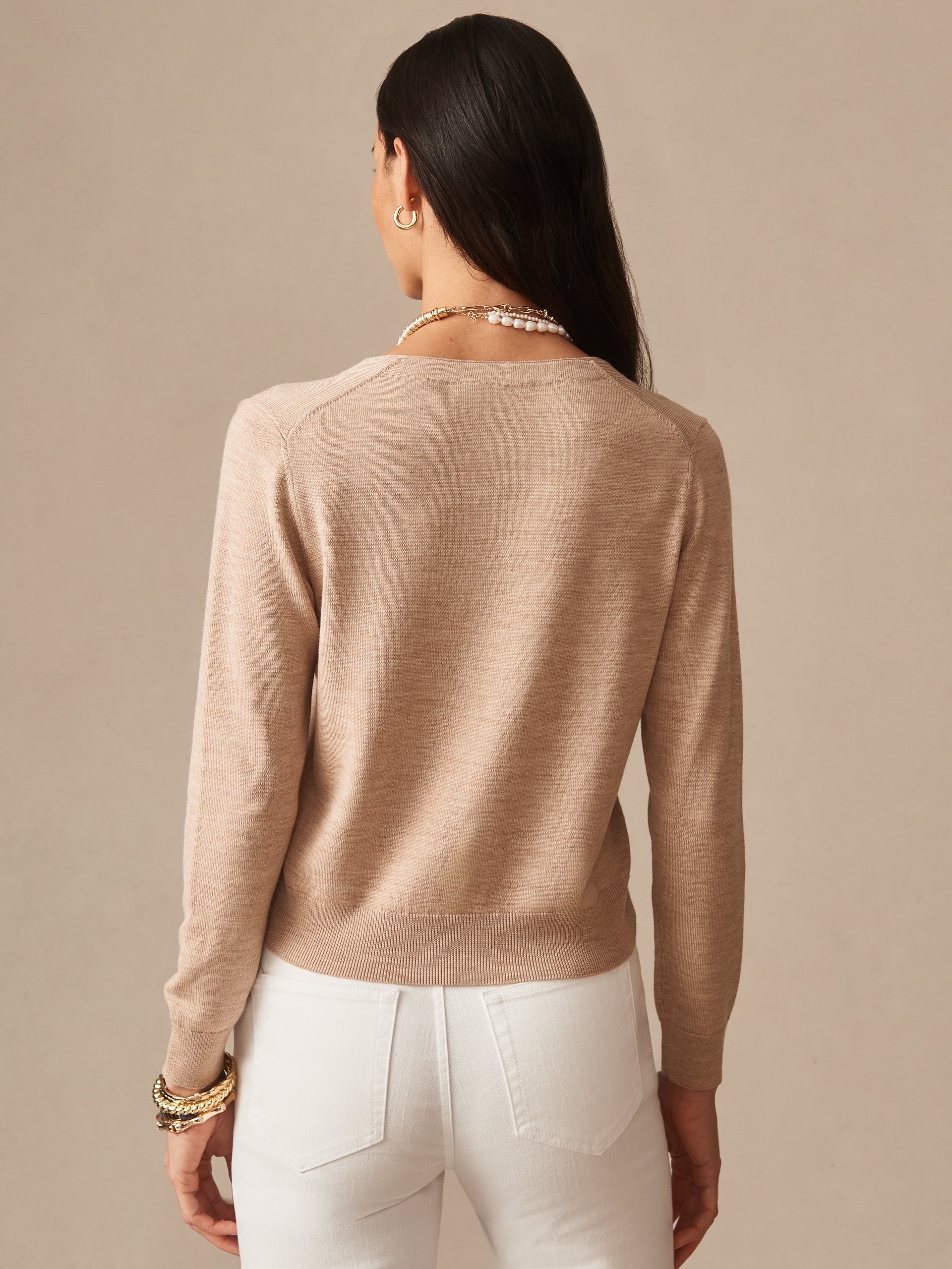 Woman shown from behind wearing a beige Olivette Cardigan by J.McLaughlin paired with white pants and gold jewelry, showcasing effortlessly stylish, enduring designs and innovative fabrics.