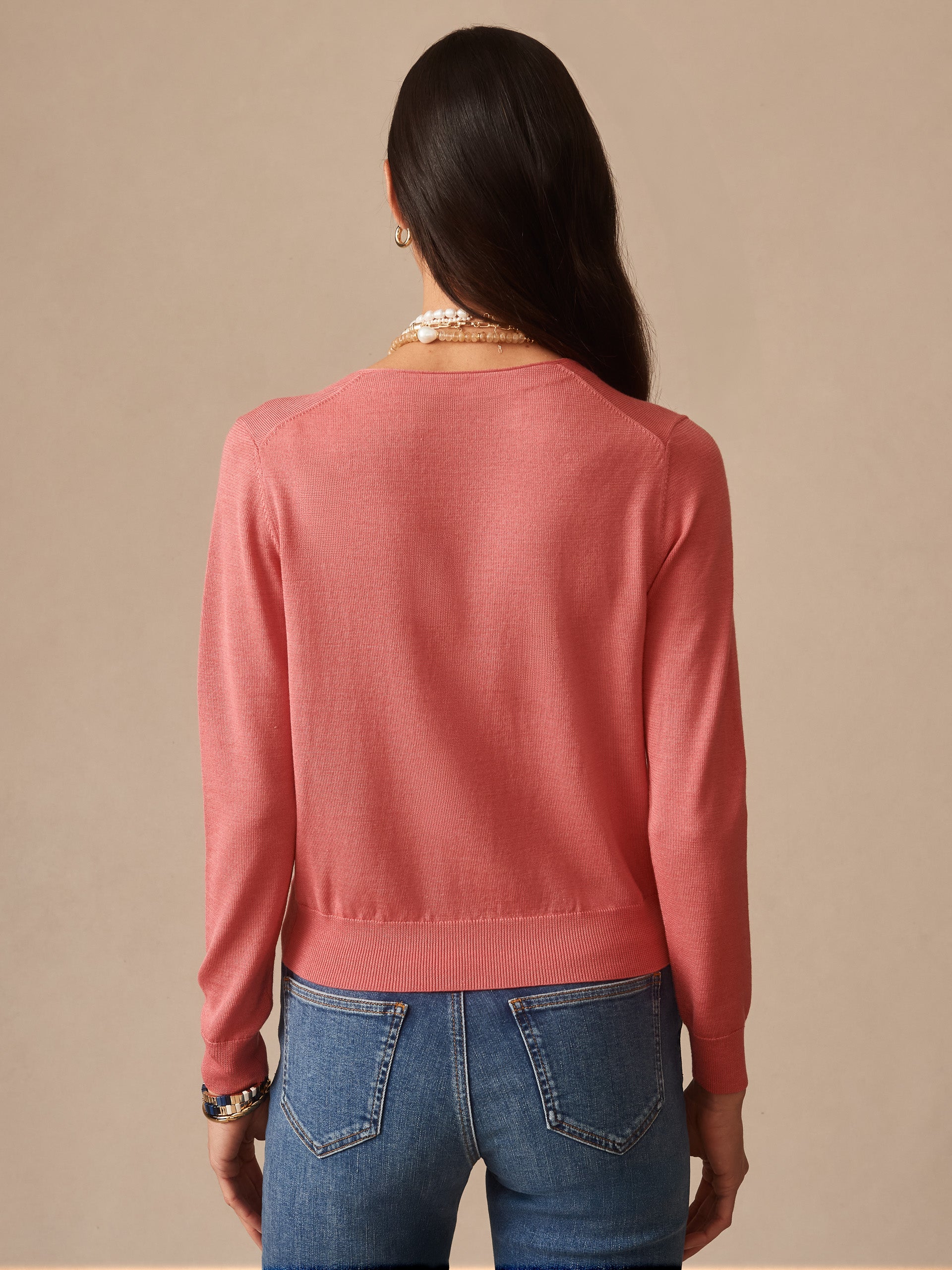 Woman wearing a soft coral Olivette Cardigan by J.McLaughlin, shown from the back with long sleeves and a fitted hem, paired with blue jeans.