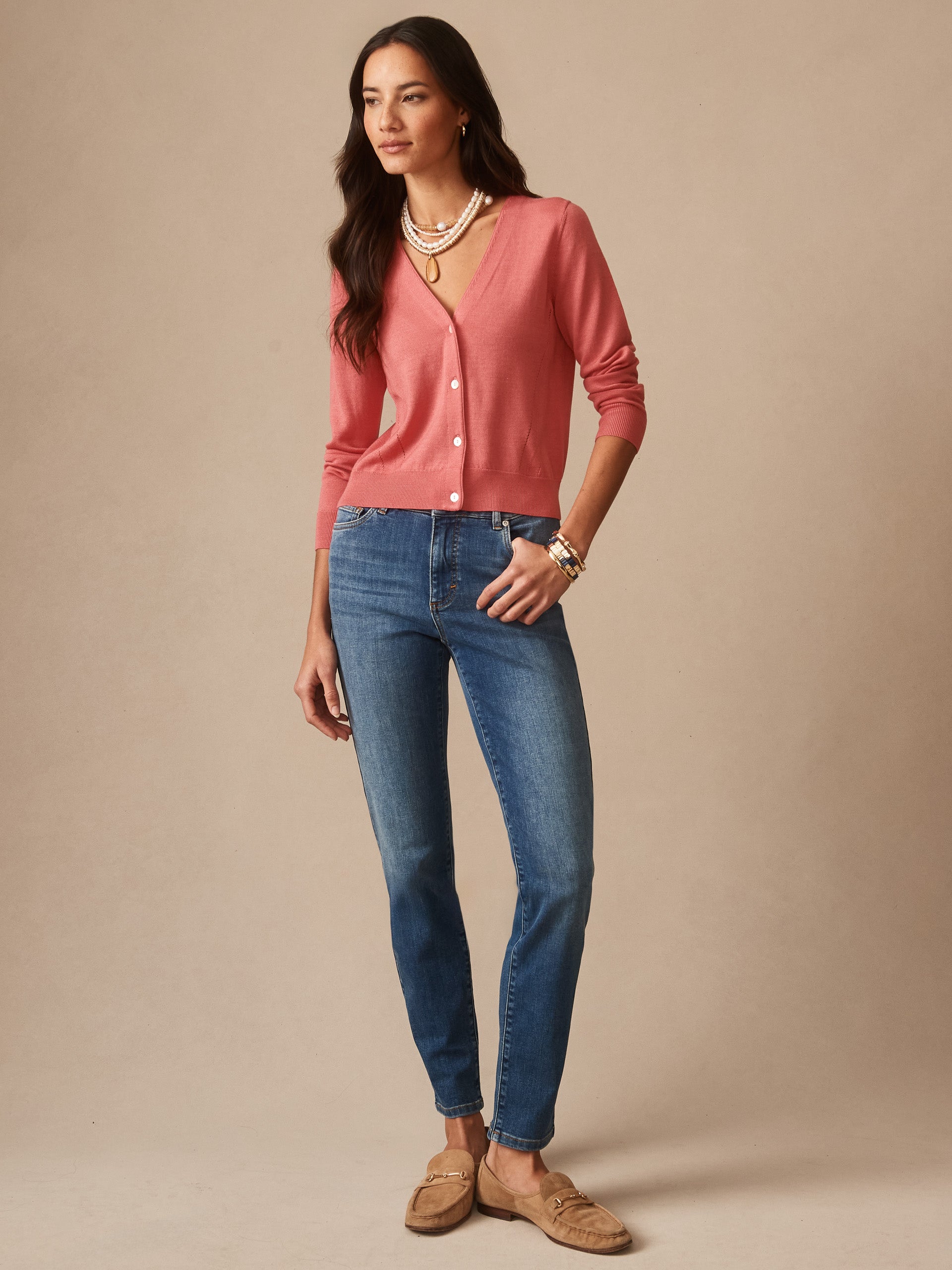Woman wearing a soft coral cardigan paired with J.McLaughlin Watson Jeans in classic indigo denim, showcasing effortlessly stylish and enduring designs for a life well-lived.