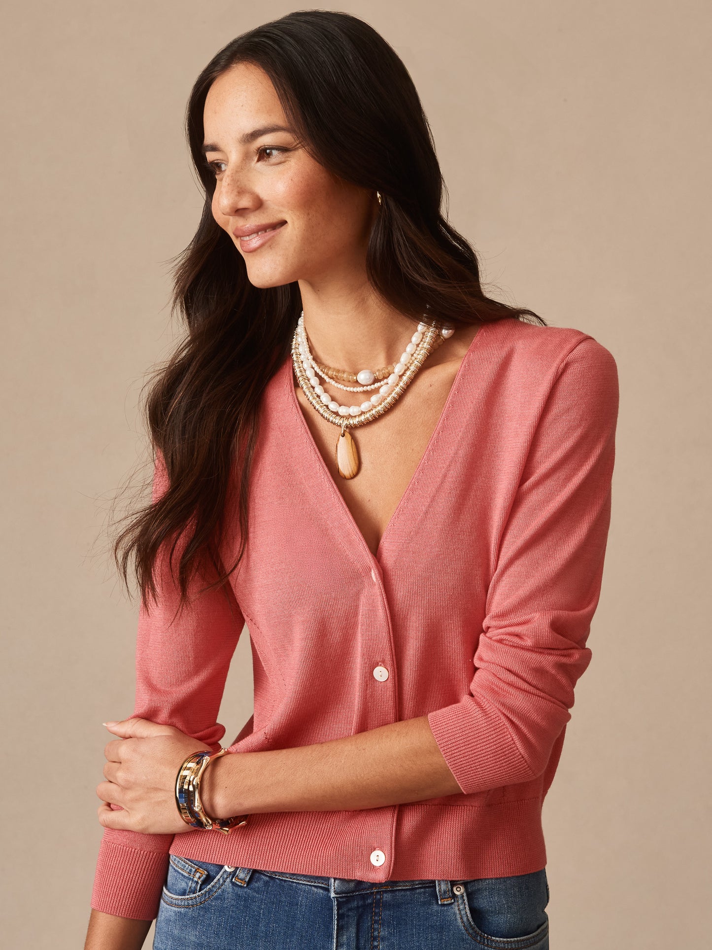 Woman wearing a soft coral Olivette Cardigan by J.McLaughlin, styled with layered pearl necklaces and casual jeans, showcasing timeless and classic craftsmanship.