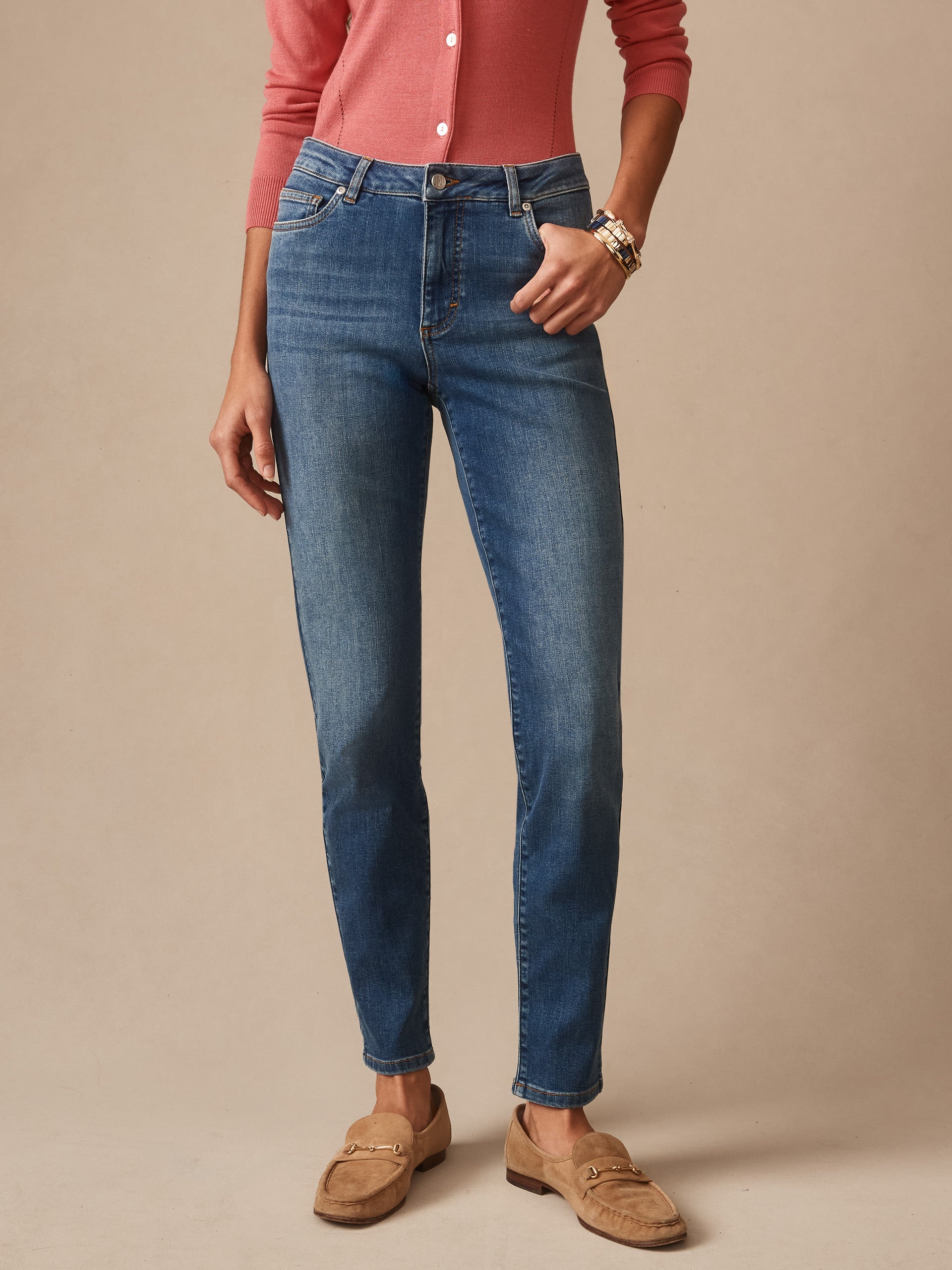 A woman wearing J. McLaughlin Watson Jeans in classic indigo paired with a coral long-sleeve top and tan loafers, embodying effortlessly stylish, enduring designs with a legacy of timeless fashion. A destination for defining style. Life, Well-Lived.