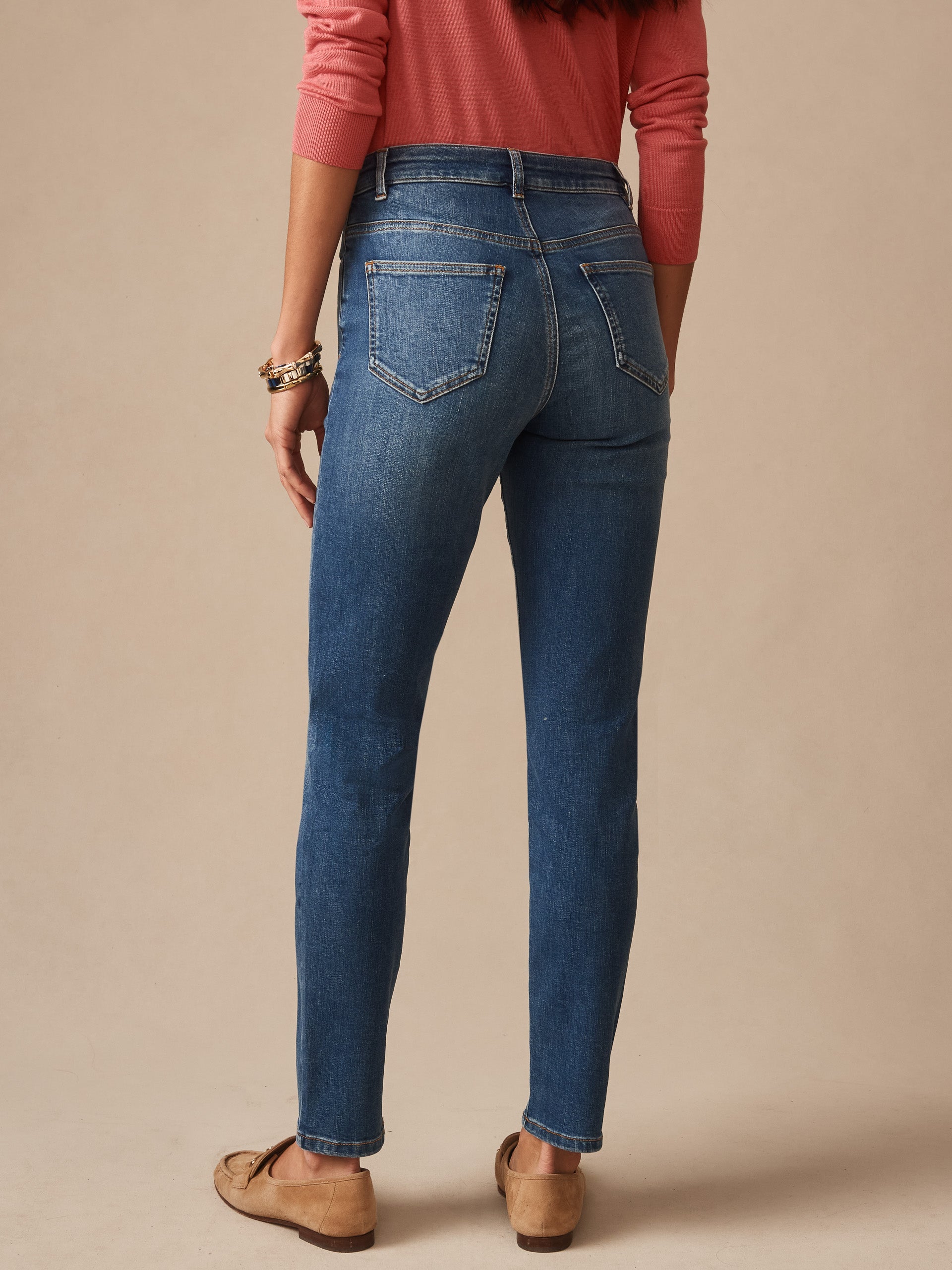 Woman wearing classic medium indigo blue Watson Jeans by J.McLaughlin, paired with casual soft coral top and brown loafers, showcasing effortlessly stylish, enduring designs with a legacy of timeless fashion. A destination for defining style. Life, Well-Lived.
