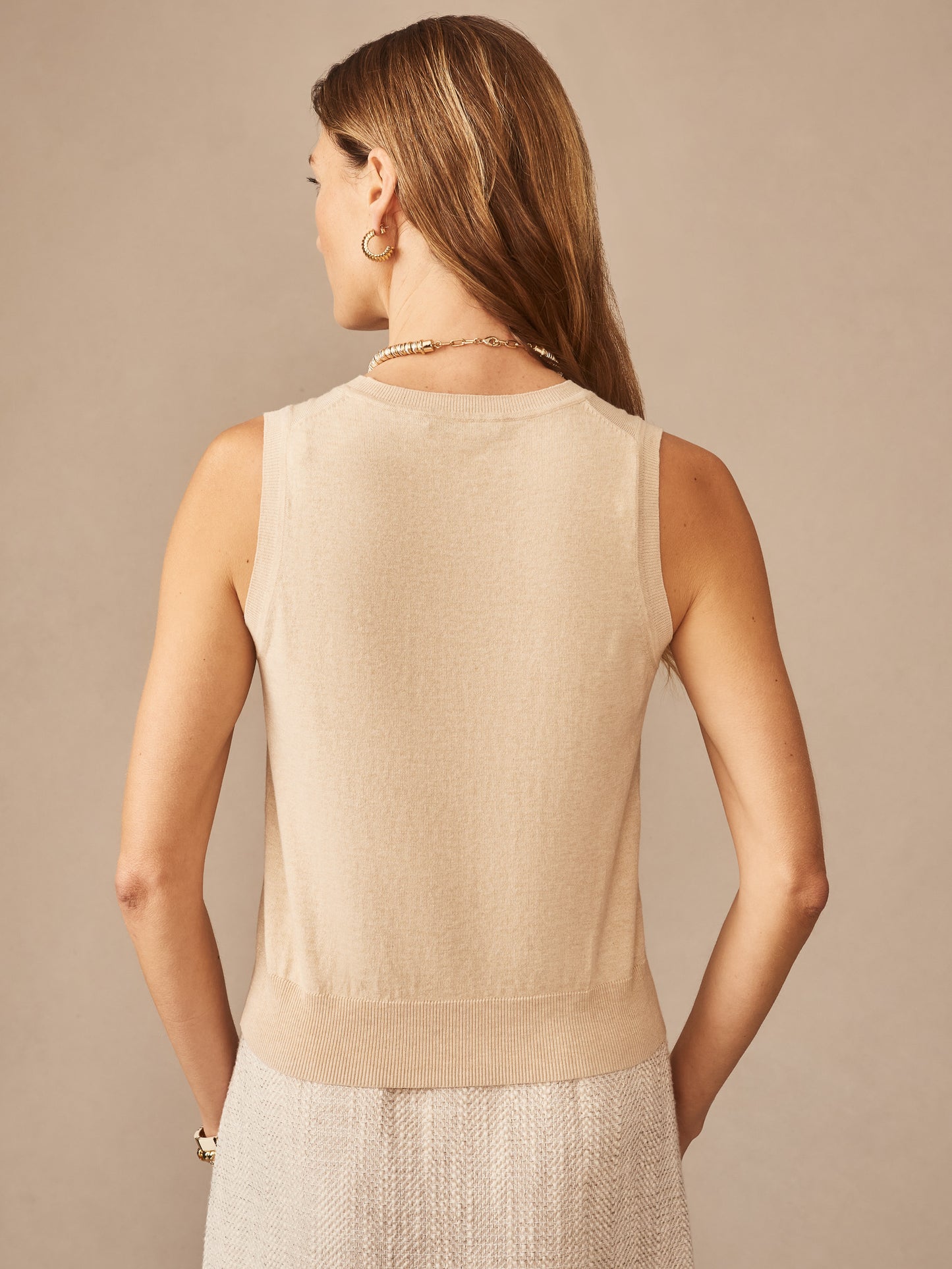 Woman wearing a beige Opal Sweater Tank by J.McLaughlin, showcasing effortlessly stylish and enduring design with innovative fabrics, embodying a legacy of timeless fashion.