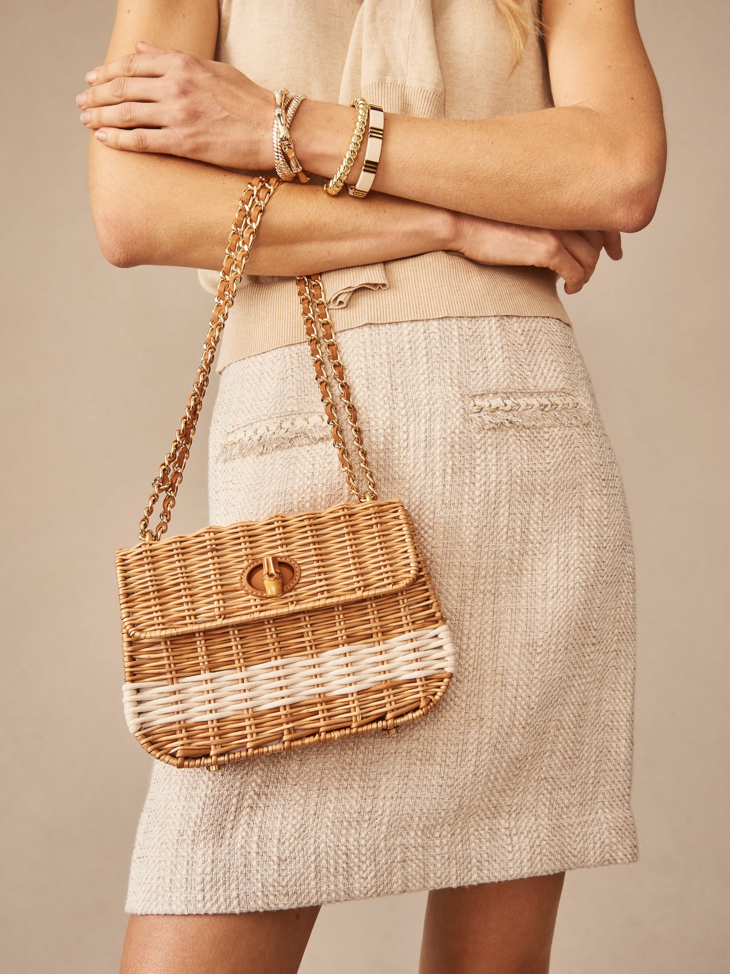 A woman wearing neutral-toned clothing holds the Waverly Wicker Handbag by J.McLaughlin, showcasing effortlessly stylish design with enduring appeal and a legacy of timeless fashion.
