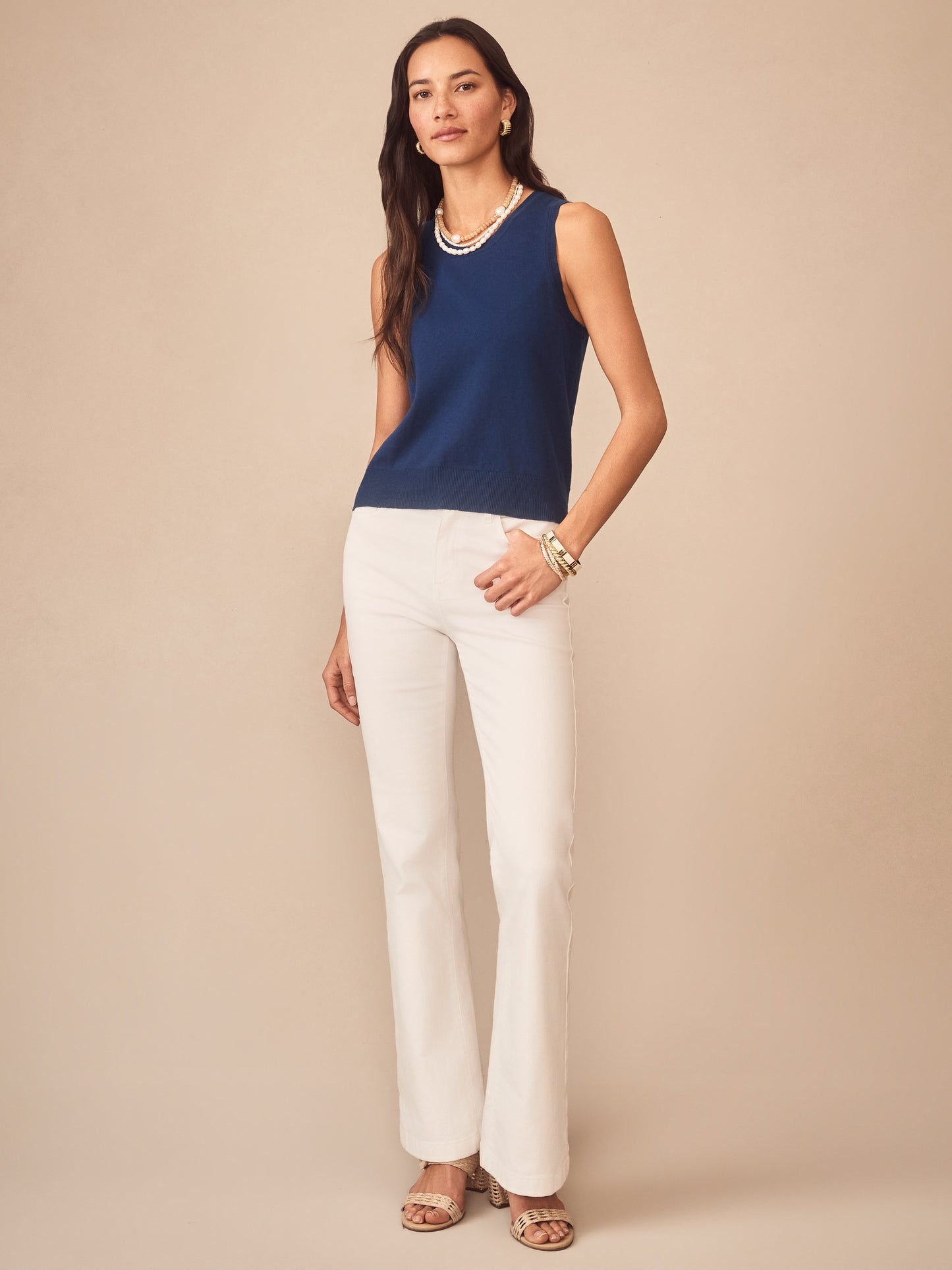 Woman wearing a nautical navy Opal Sweater Tank by J.McLaughlin paired with white pants and layered pearl necklace, showcasing effortlessly stylish, enduring designs and innovative fabrics.