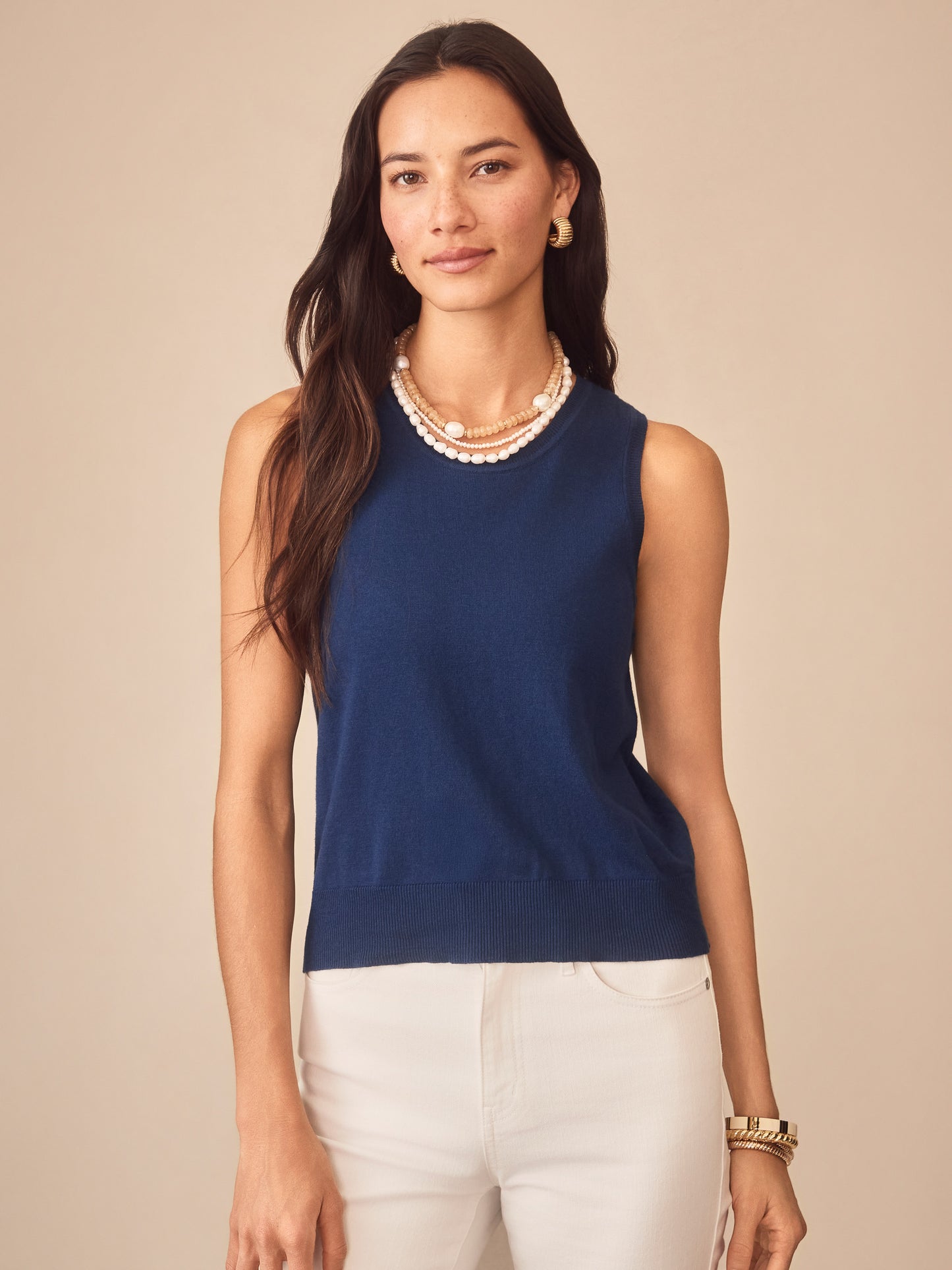 Woman wearing a nautical navy Opal Sweater Tank by J.McLaughlin paired with white pants and layered pearl necklaces, showcasing effortlessly stylish, enduring designs and innovative fabrics.