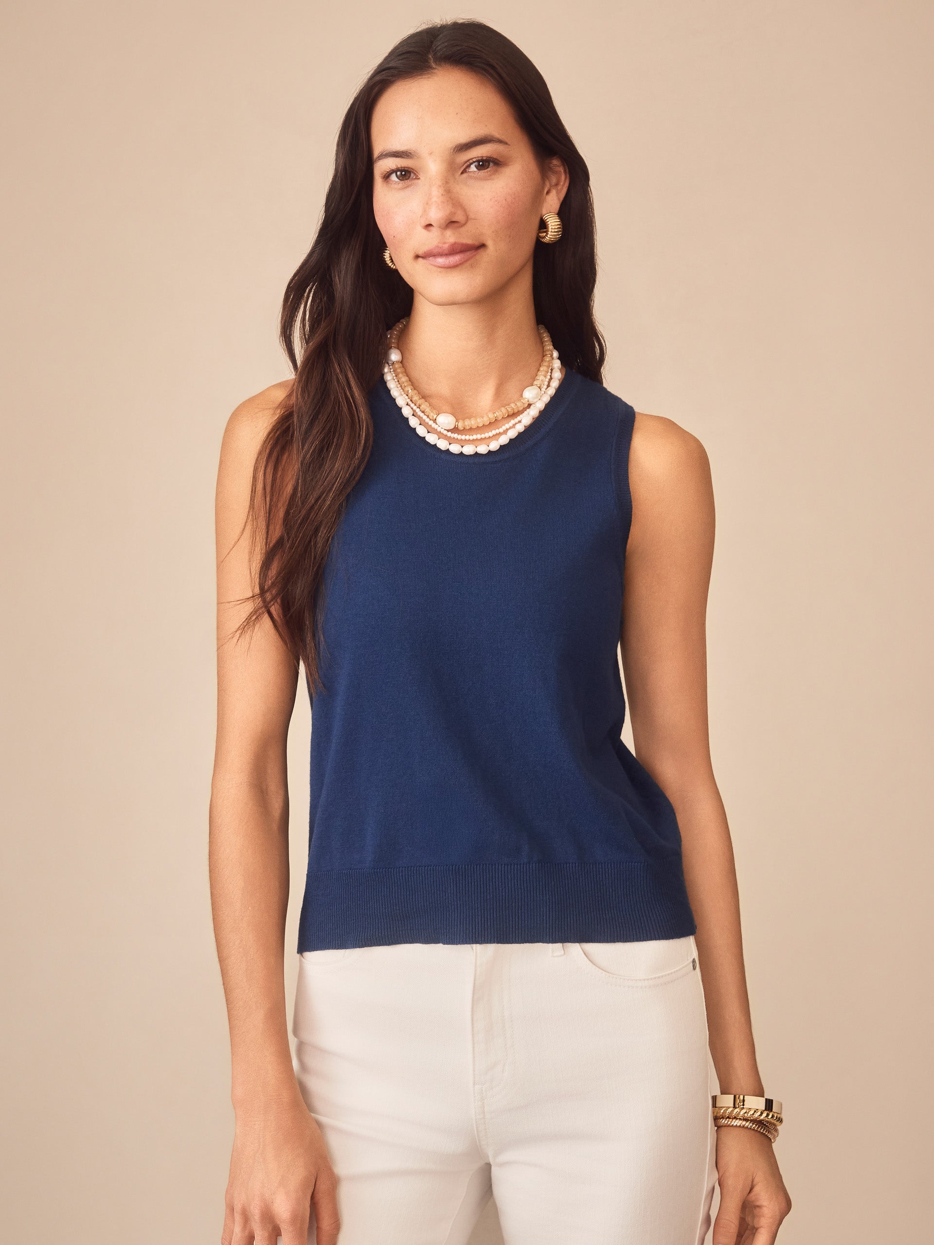 Woman wearing a nautical navy Opal Sweater Tank by J.McLaughlin paired with white pants and layered pearl necklaces, showcasing effortlessly stylish, enduring designs and innovative fabrics.