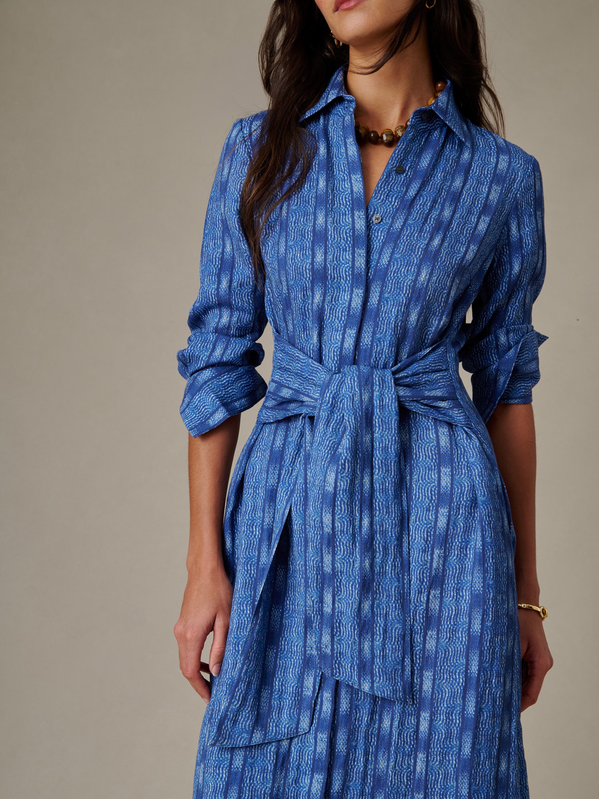 Close-up of a woman wearing the Orla Dress in Wavelength by J.McLaughlin, featuring a blue patterned fabric, button-up front, and tied waist belt, showcasing timeless style and quality craftsmanship.