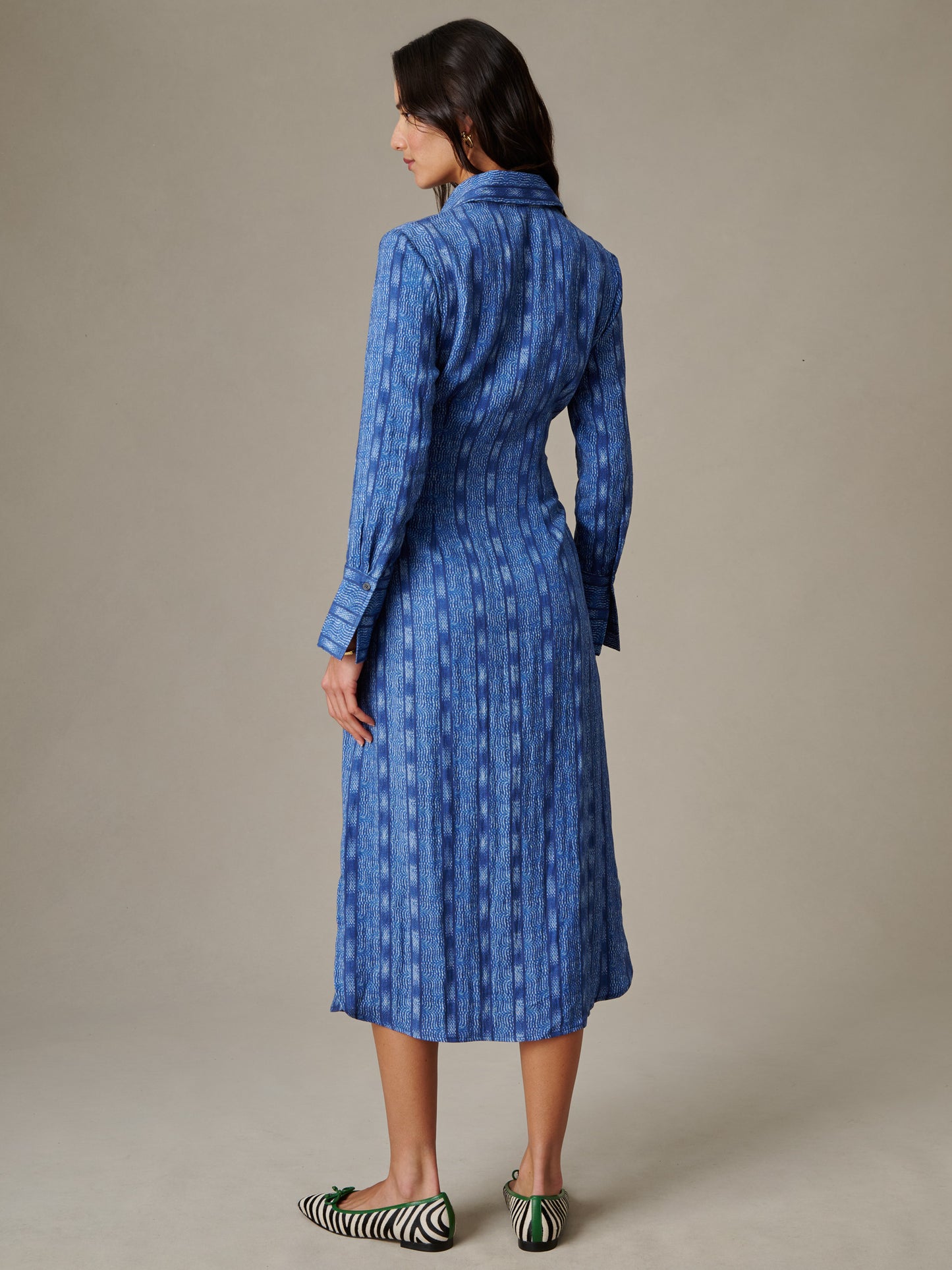 Woman modeling the Orla Dress in Wavelength by J.McLaughlin, showcasing a classic, timeless blue patterned dress with long sleeves and a midi length, paired with striped flats.