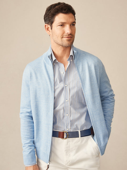 Man wearing a light blue Orwell Sweater by J.McLaughlin over a striped shirt paired with white pants and a striped belt, showcasing effortlessly stylish, enduring designs and innovative fabrics.